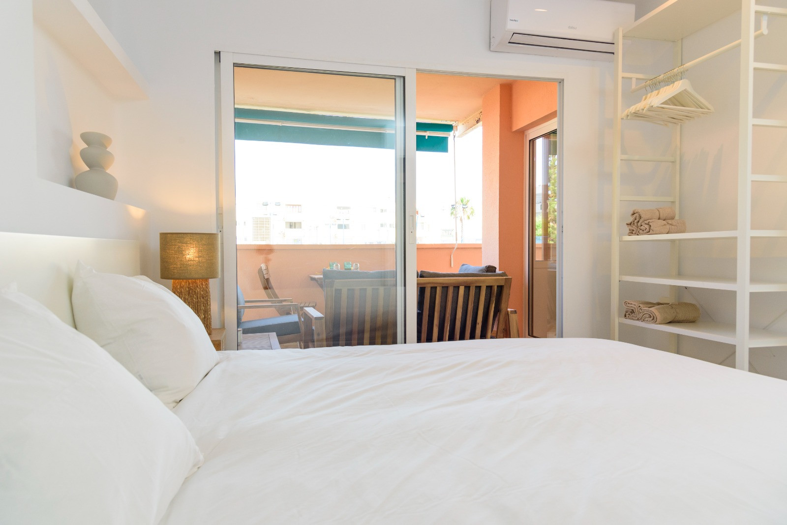 Helles Schlafzimmer mit direktem Zugang zur möblierten Terrasse, offenem Regalsystem im minimalistischen Design und Split-Klimaanlage.