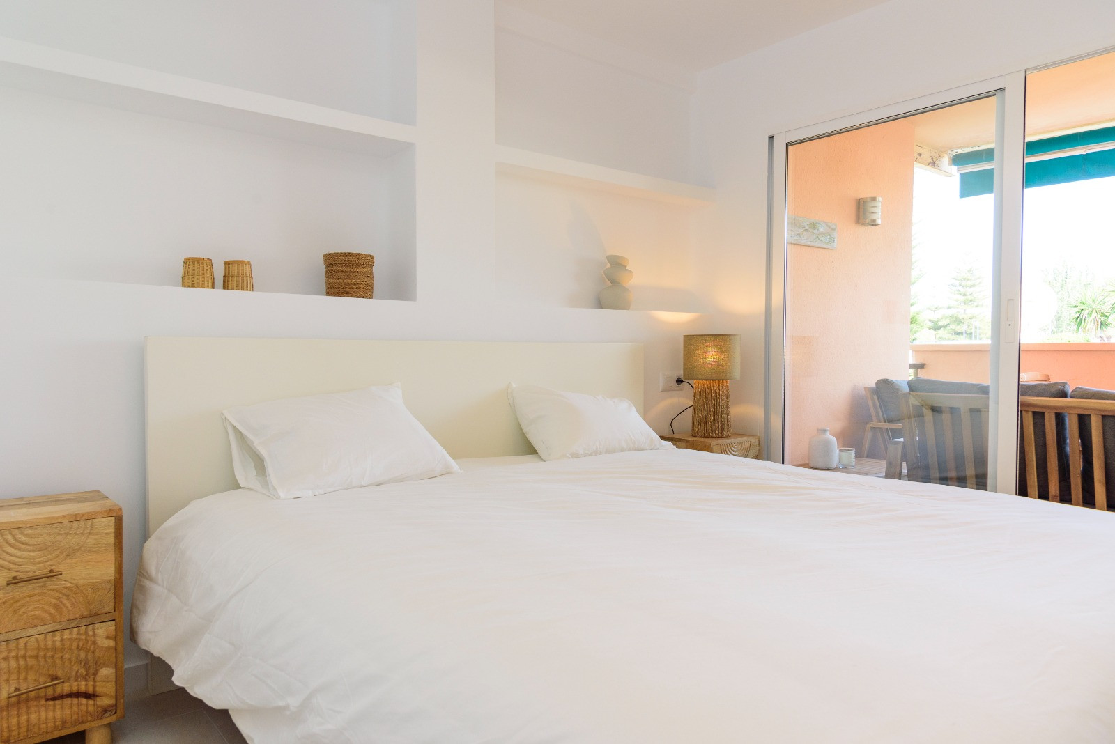 Helles Schlafzimmer mit integrierten Wandregalen, Nachttischen aus Holz und direktem Zugang zur privaten Terrasse durch große Glasschiebetüren.