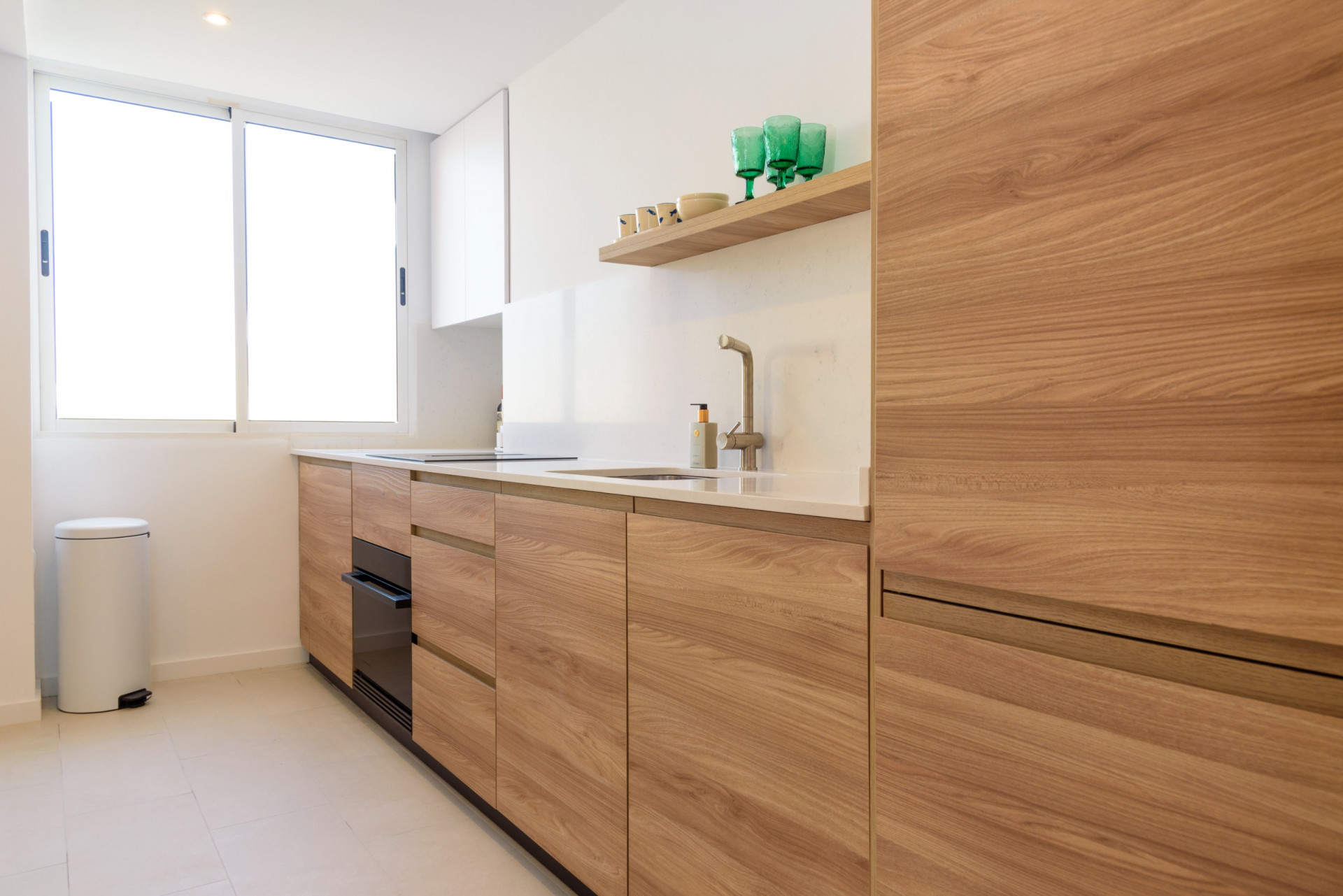 Moderne Küche mit Holzfronten, weißer Arbeitsplatte und integrierter Spüle. Ein großes Fenster sorgt für viel natürliches Licht und betont das zeitgemäße, funktionale Design.