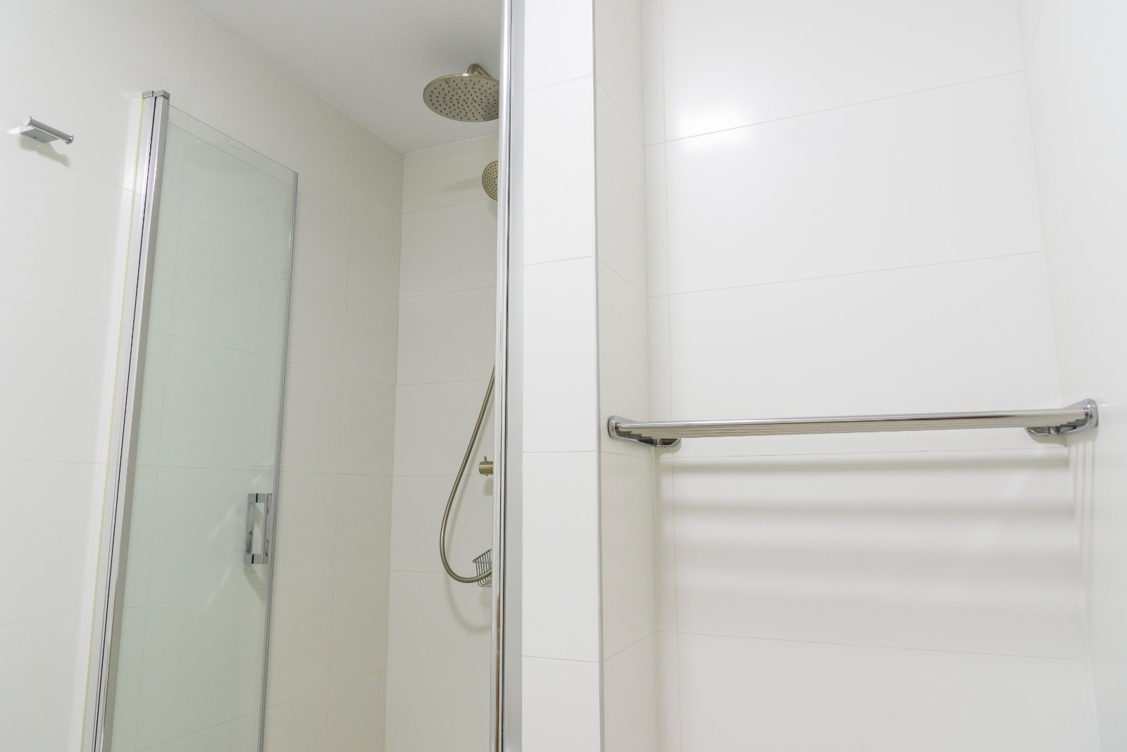 Modernes Badezimmer mit begehbarer Dusche, Glastür und verchromten Armaturen inklusive Regenduschkopf. Weiße Wandfliesen und ein integrierter Handtuchhalter aus Metall.