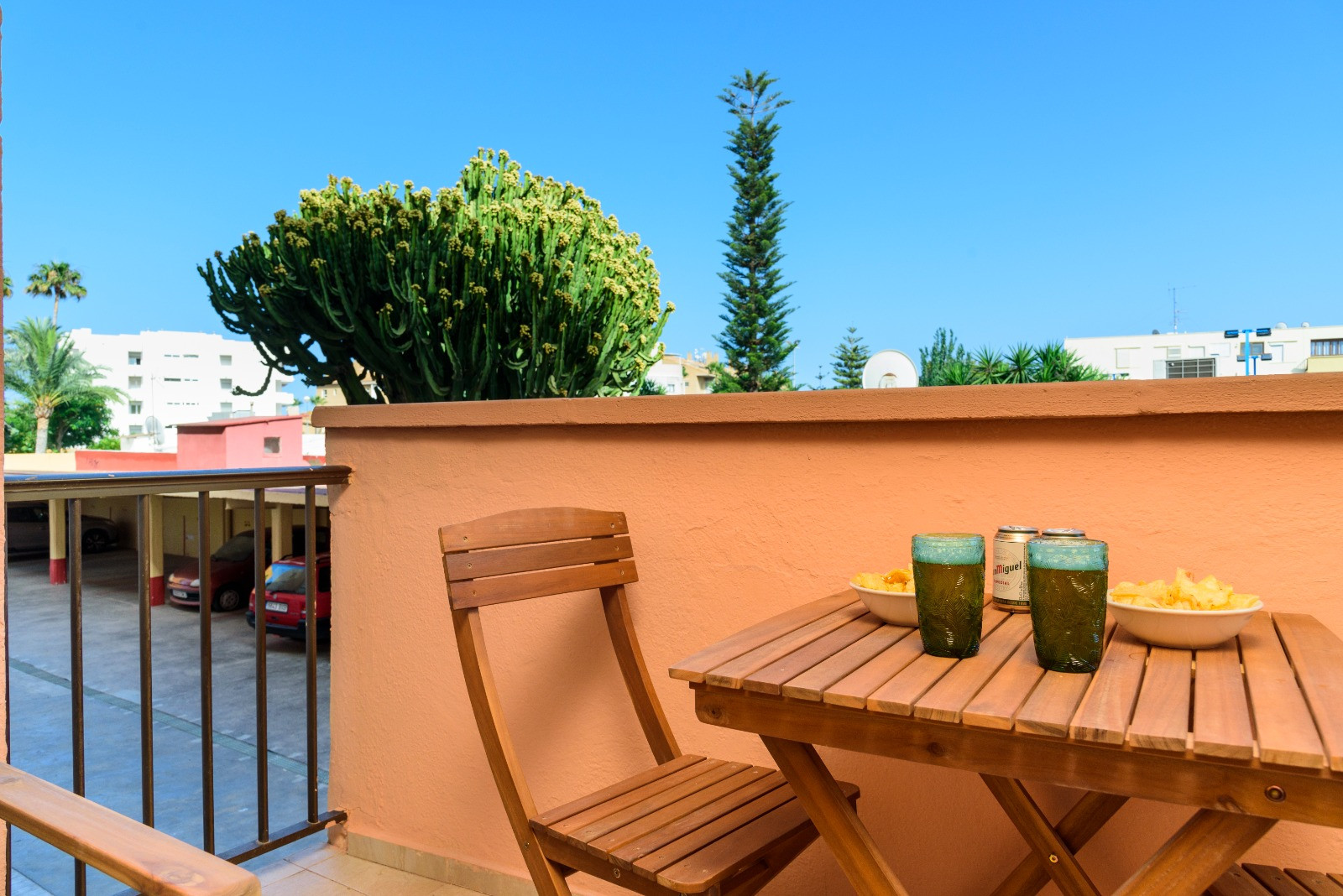 Private Terrasse mit Holzmöbeln, ideal für Snacks im Freien. Sie bietet einen Blick auf Gartenbereiche mit Kakteen und Palmen unter strahlend blauem Himmel.