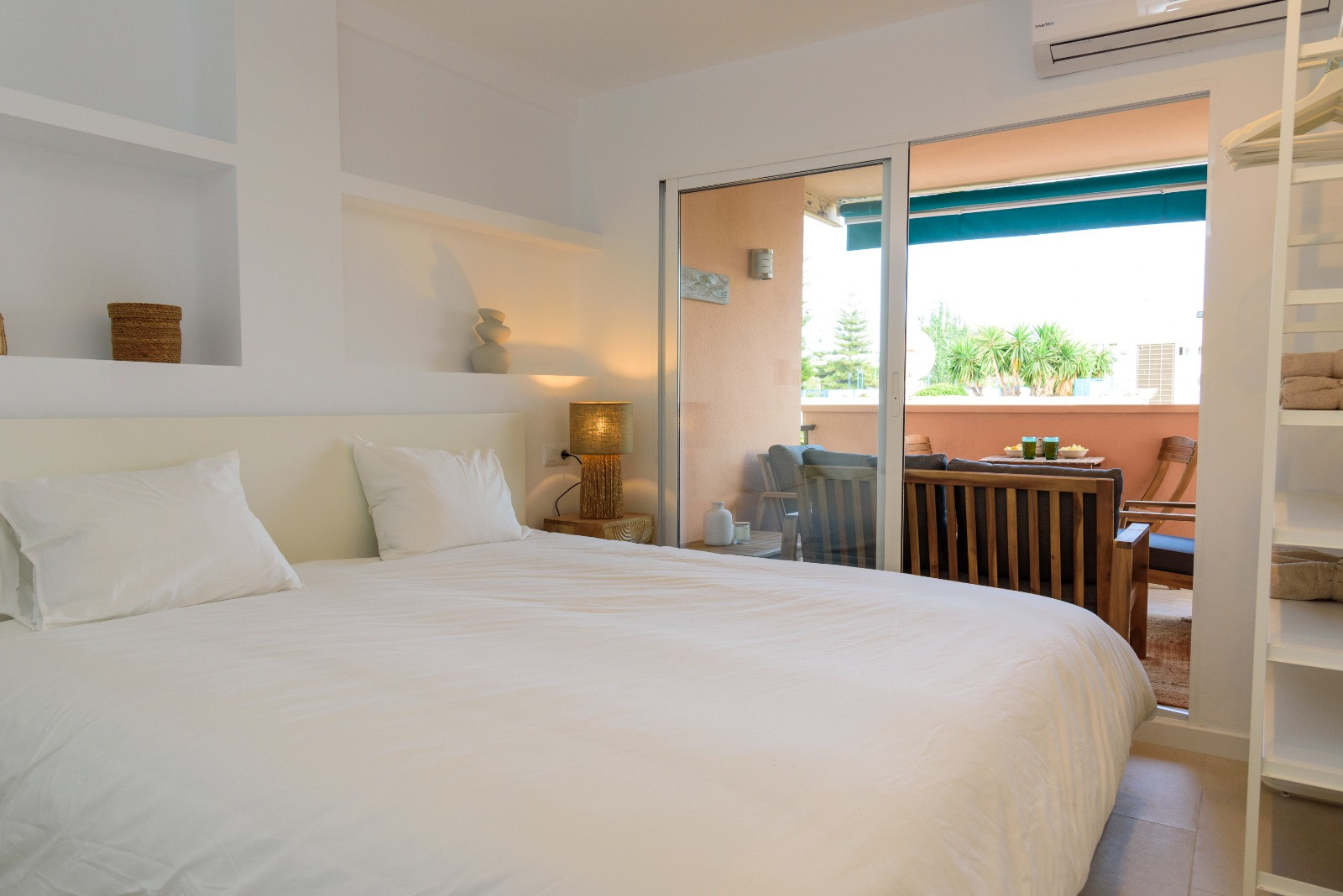 Schlafzimmer mit integrierten Wandregalen und Glasschiebetüren, die auf eine möblierte Terrasse führen und für viel natürliches Licht sorgen.