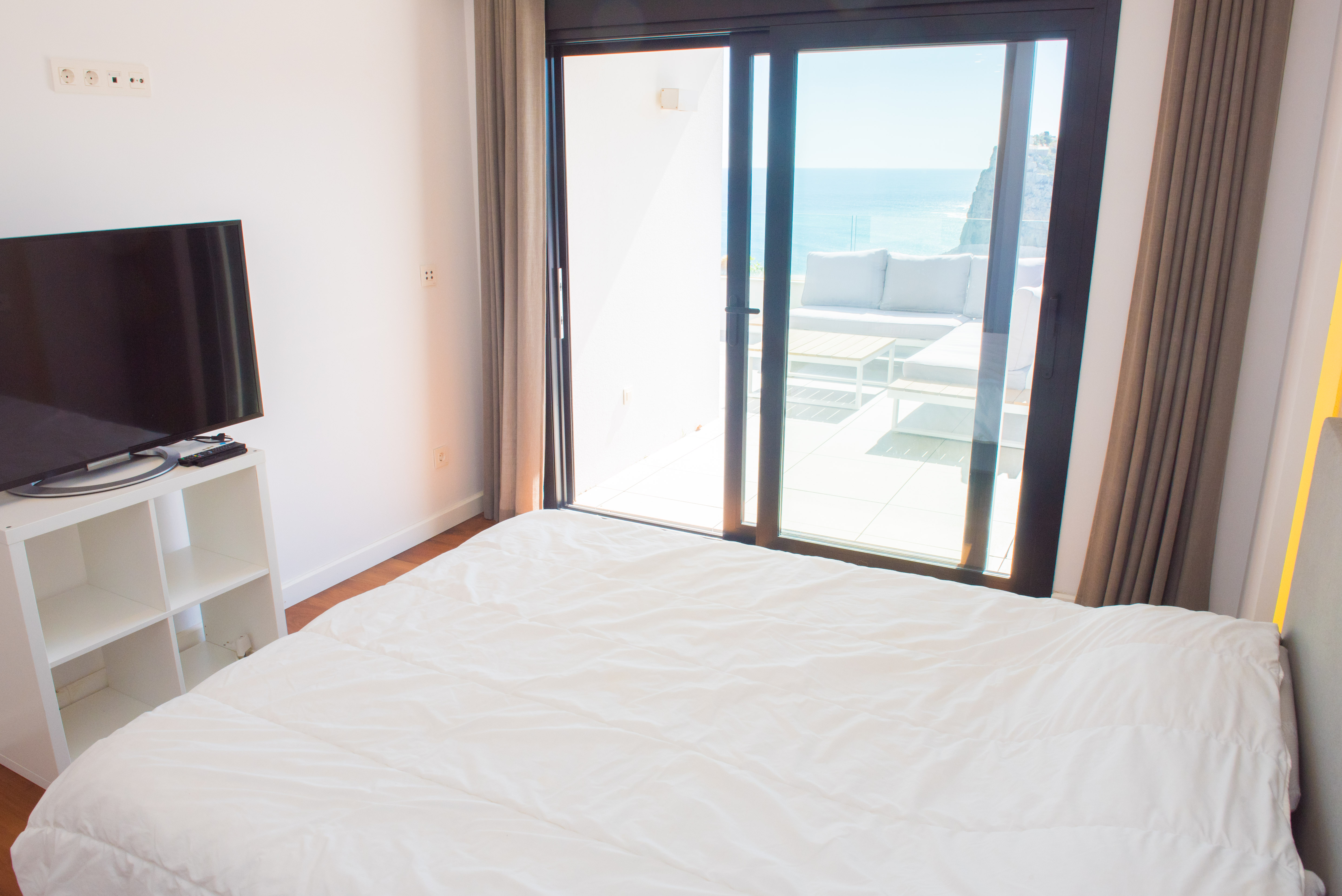 Helles Schlafzimmer mit direktem Zugang zur privaten Terrasse mit Loungemöbeln und weitem Panoramablick auf das Mittelmeer und die Küstenfelsen.