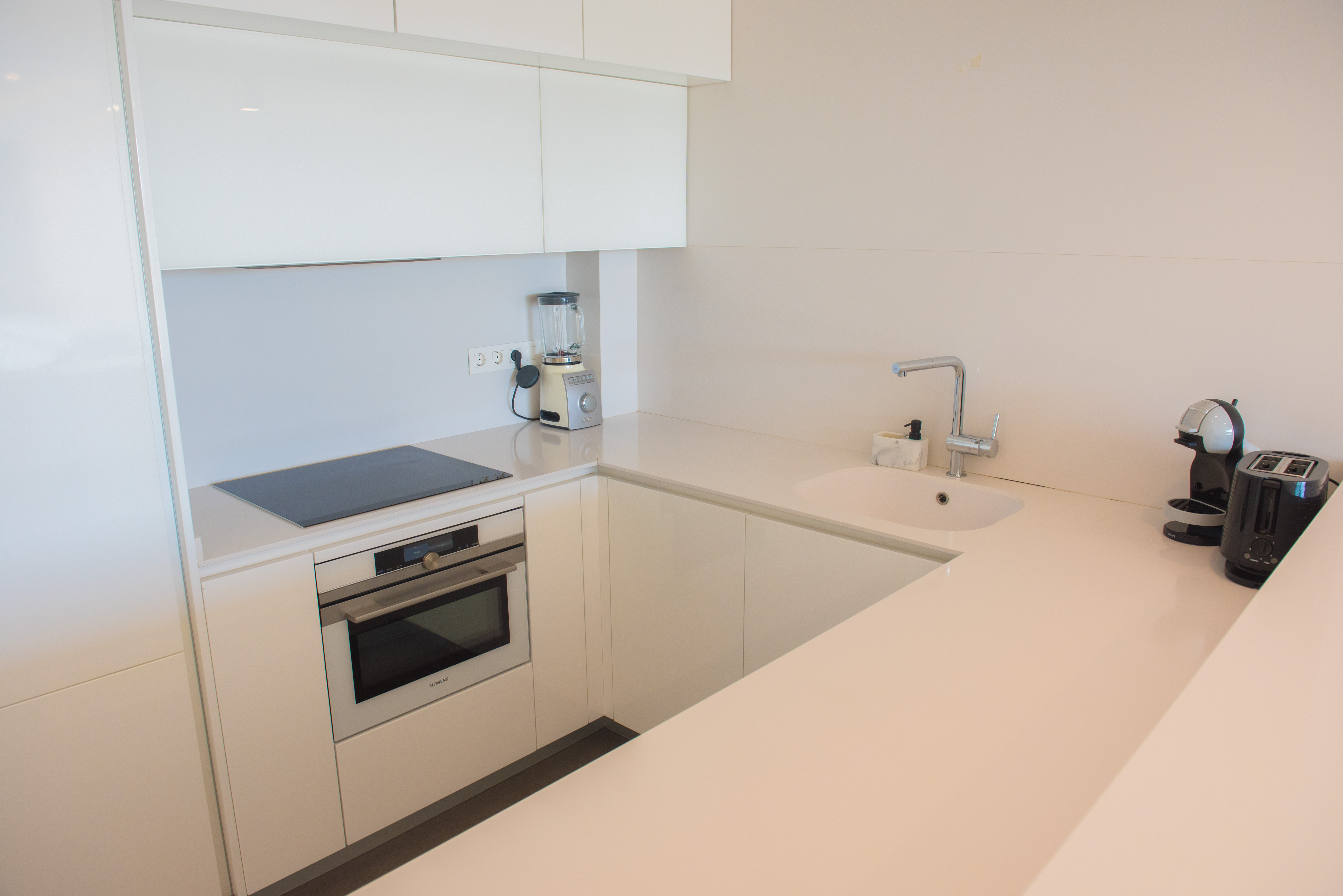 Minimalistische Hochglanzküche in Weiß mit Quarz-Arbeitsplatte, Siemens-Backofen, Induktionsfeld und hochwertigen Küchengeräten in U-Form-Anordnung.