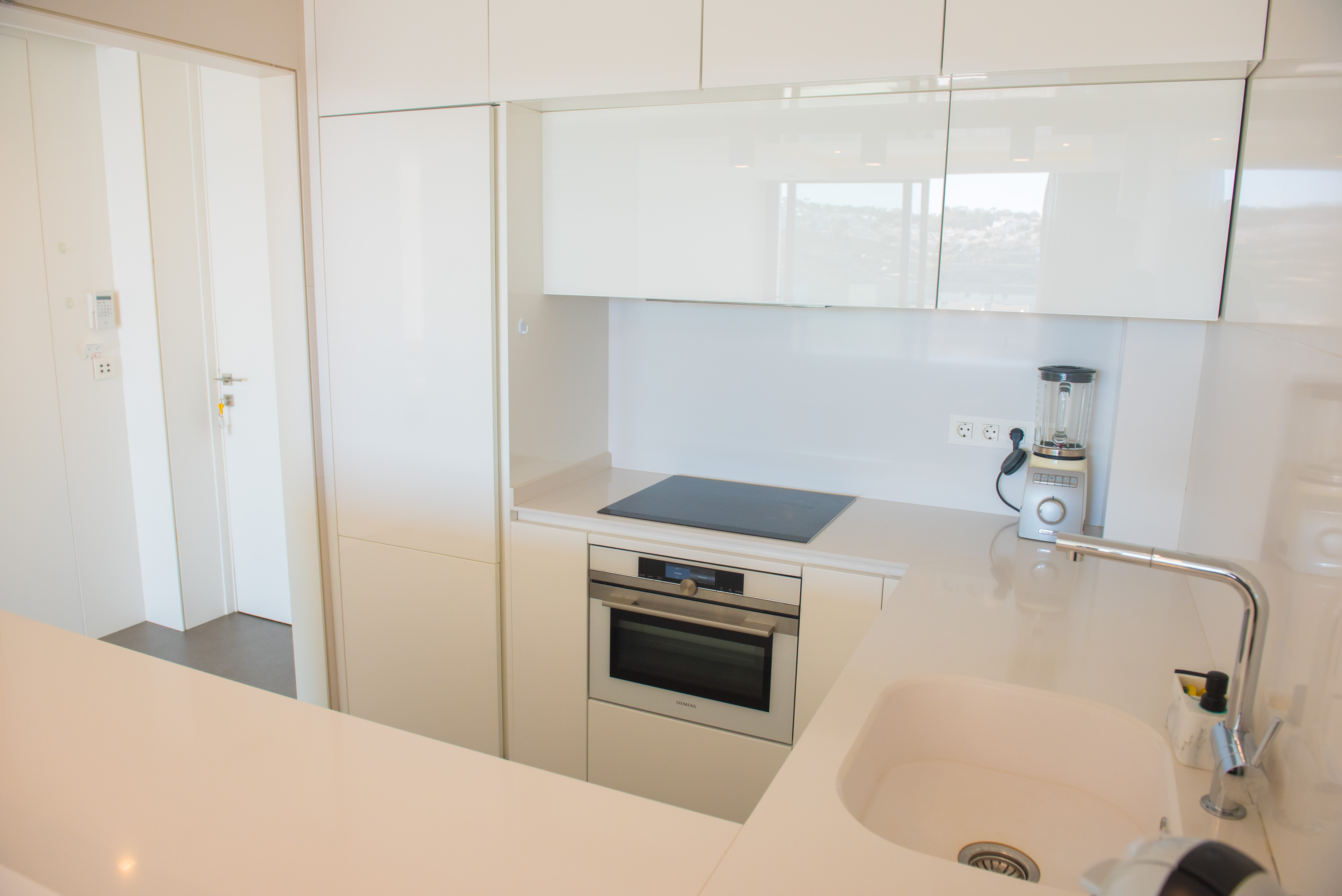 Moderne Küche mit hochglänzenden weißen Schränken, integriertem Siemens-Backofen, Induktionskochfeld und weißer Quarz-Arbeitsplatte mit Unterbauspüle.