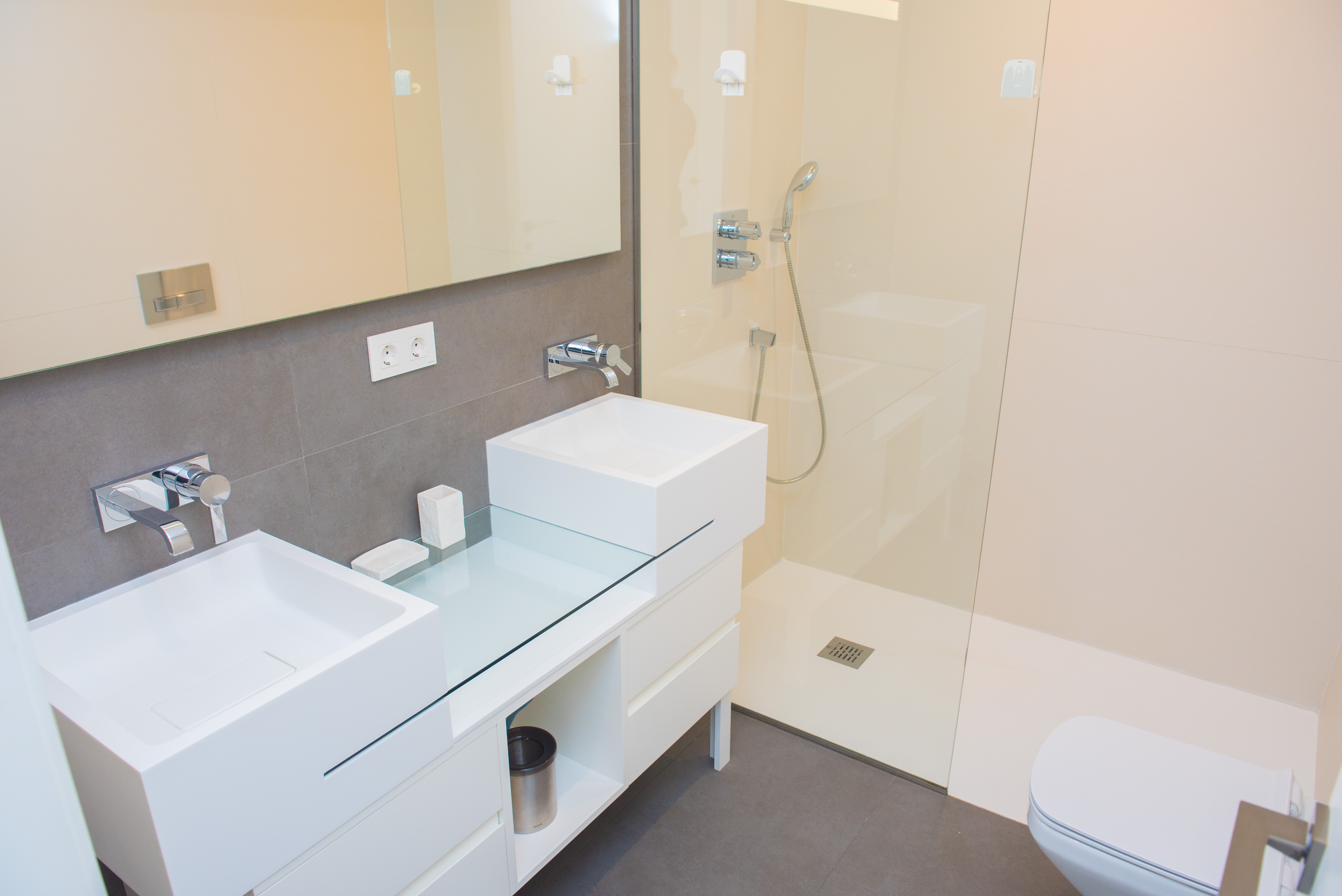 Modernes Badezimmer mit Doppelwaschtisch, quadratischen Aufsatzbecken, Unterputz-Armaturen und einer begehbaren Dusche mit Glasabtrennung.