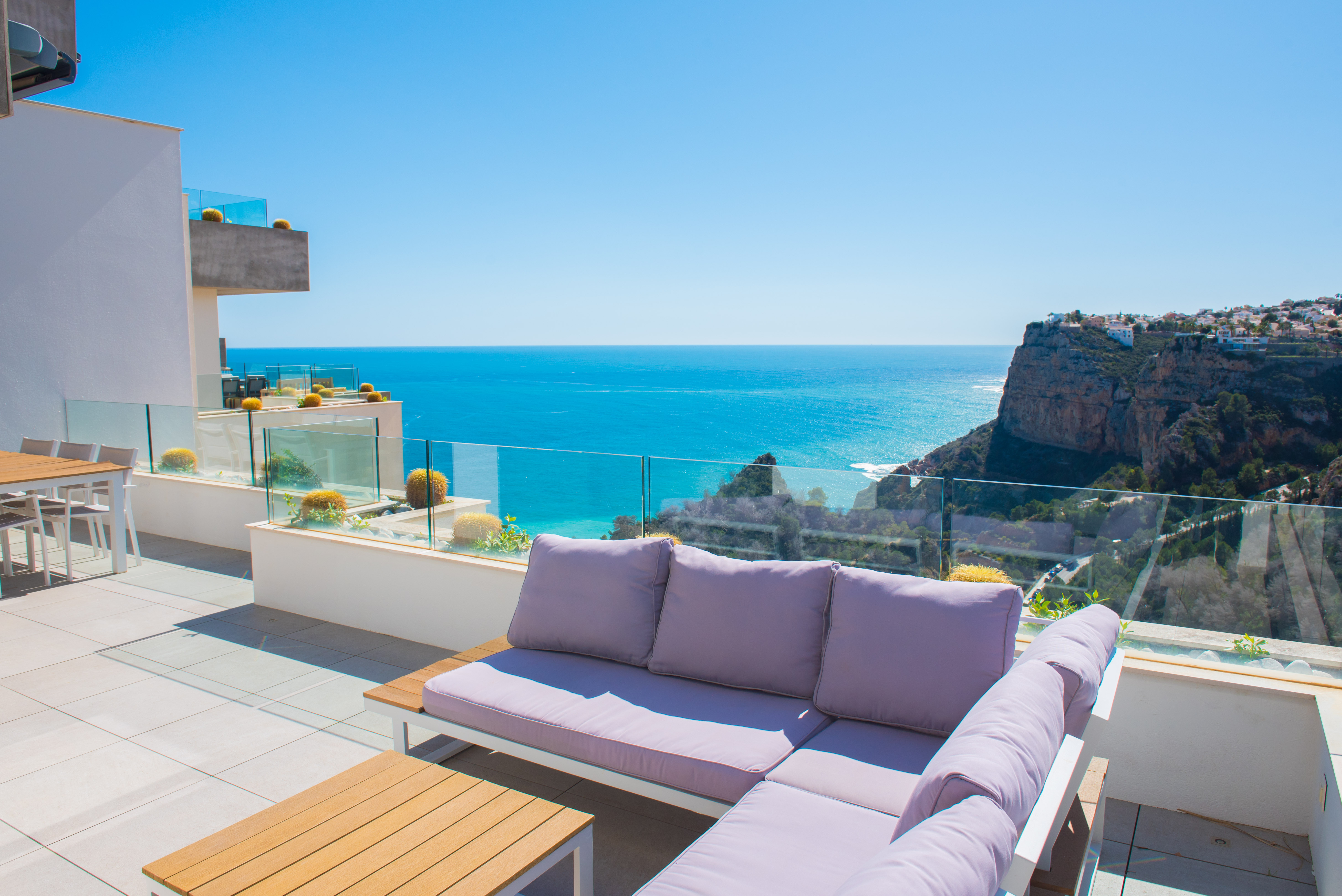 Private Terrasse mit L-förmigem Sofa, Glasgeländern und Panoramablick auf das Mittelmeer und die angrenzenden Klippen.