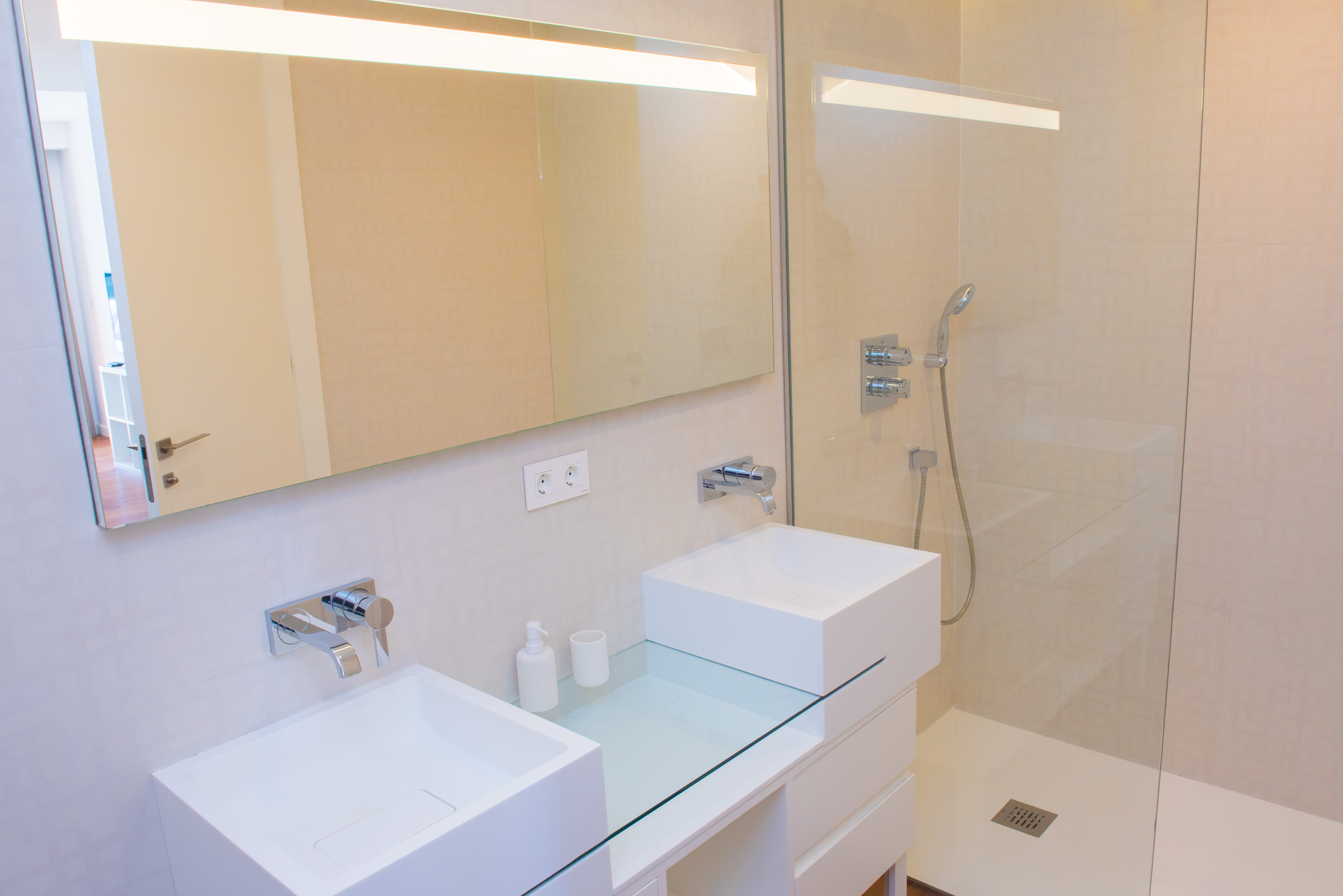 Zeitgenössisches Badezimmer mit Doppelwaschbecken, Unterputz-Armaturen und einer ebenerdigen Dusche mit Glastrennwand und LED-beleuchtetem Spiegel.