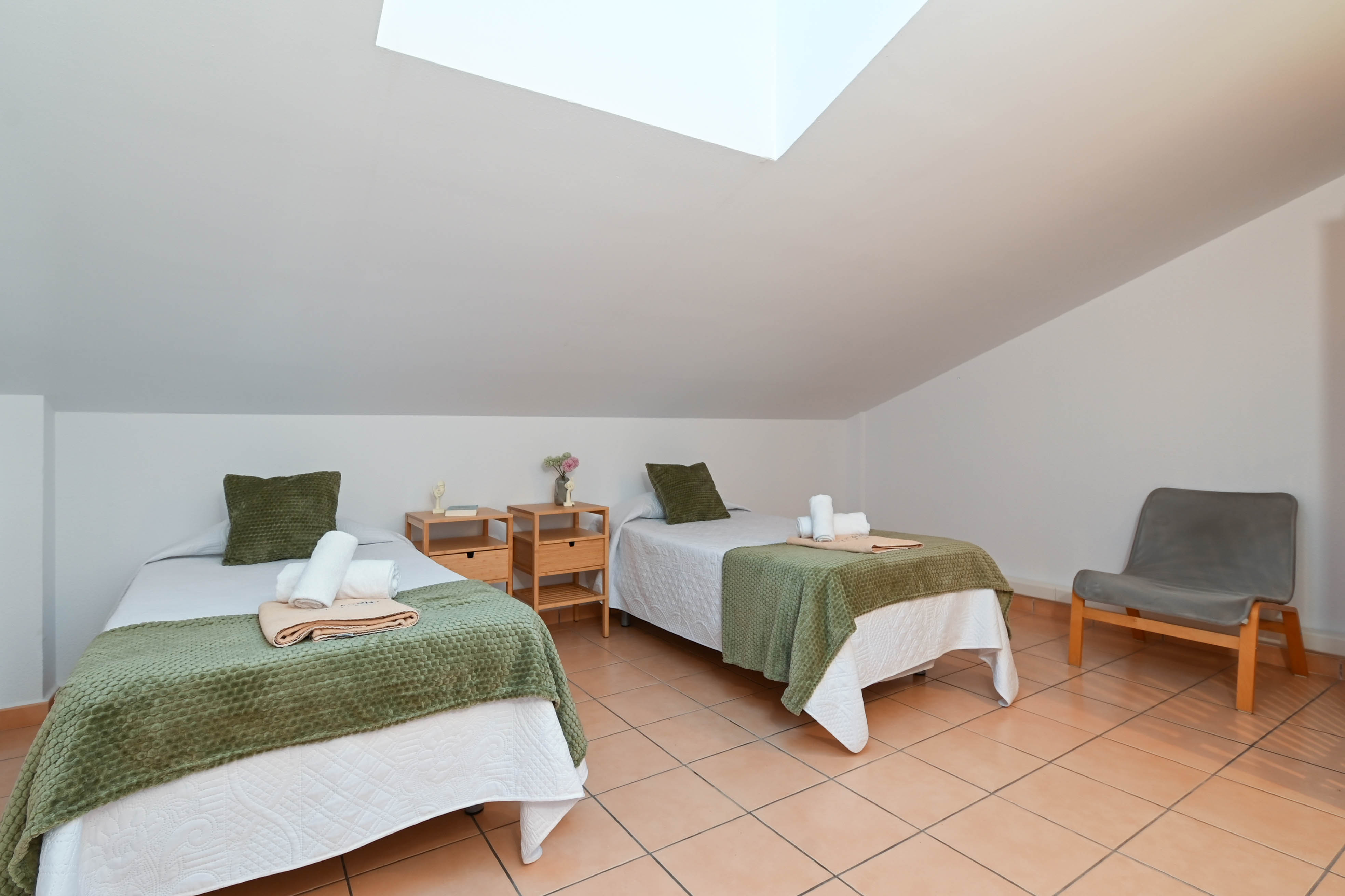 Dachgeschoss-Schlafzimmer mit zwei Einzelbetten, Terrakotta-Fliesenboden und einem Dachfenster, das für helles, natürliches Licht sorgt.