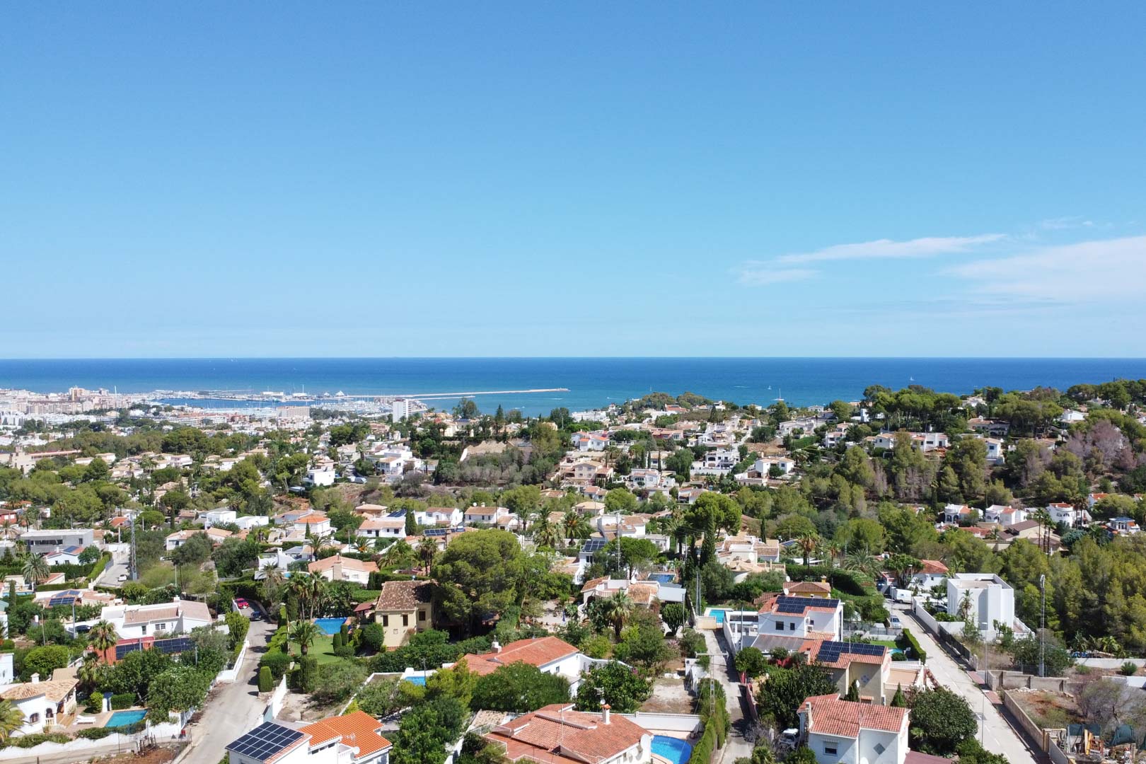 Panorama-Luftaufnahme des Wohngebiets von Dénia mit Blick auf das Mittelmeer, den Hafen und eine gewachsene Siedlung aus Einfamilienhäusern mit Pools.