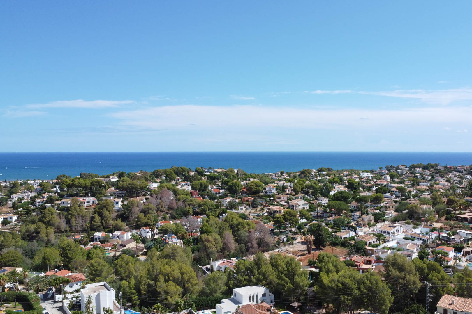 Panorama-Luftaufnahme eines Wohnviertels in Dénia mit weißen Villen inmitten von Pinienwäldern und direktem Blick auf den Horizont des Mittelmeers.