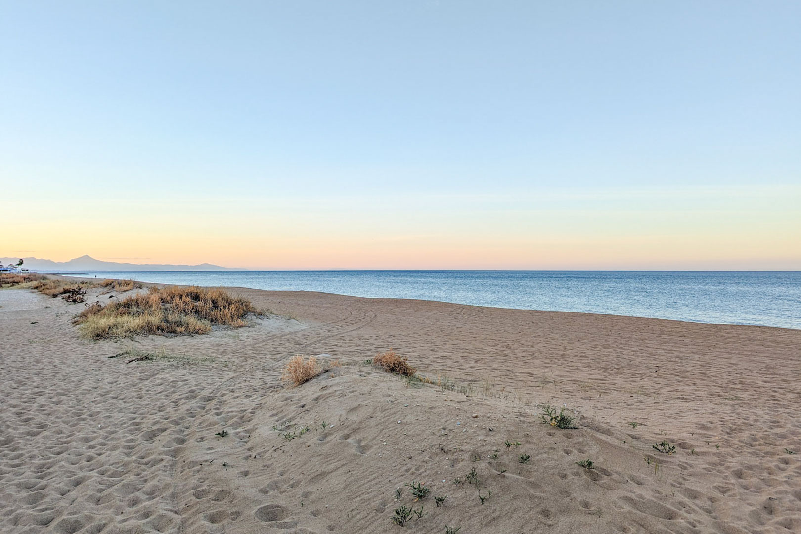 Breiter Sandstrand mit natürlichen Dünen und einheimischer Vegetation nahe der Immobilie. Blick auf das Mittelmeer und ferne Bergsilhouetten in der Abenddämmerung.