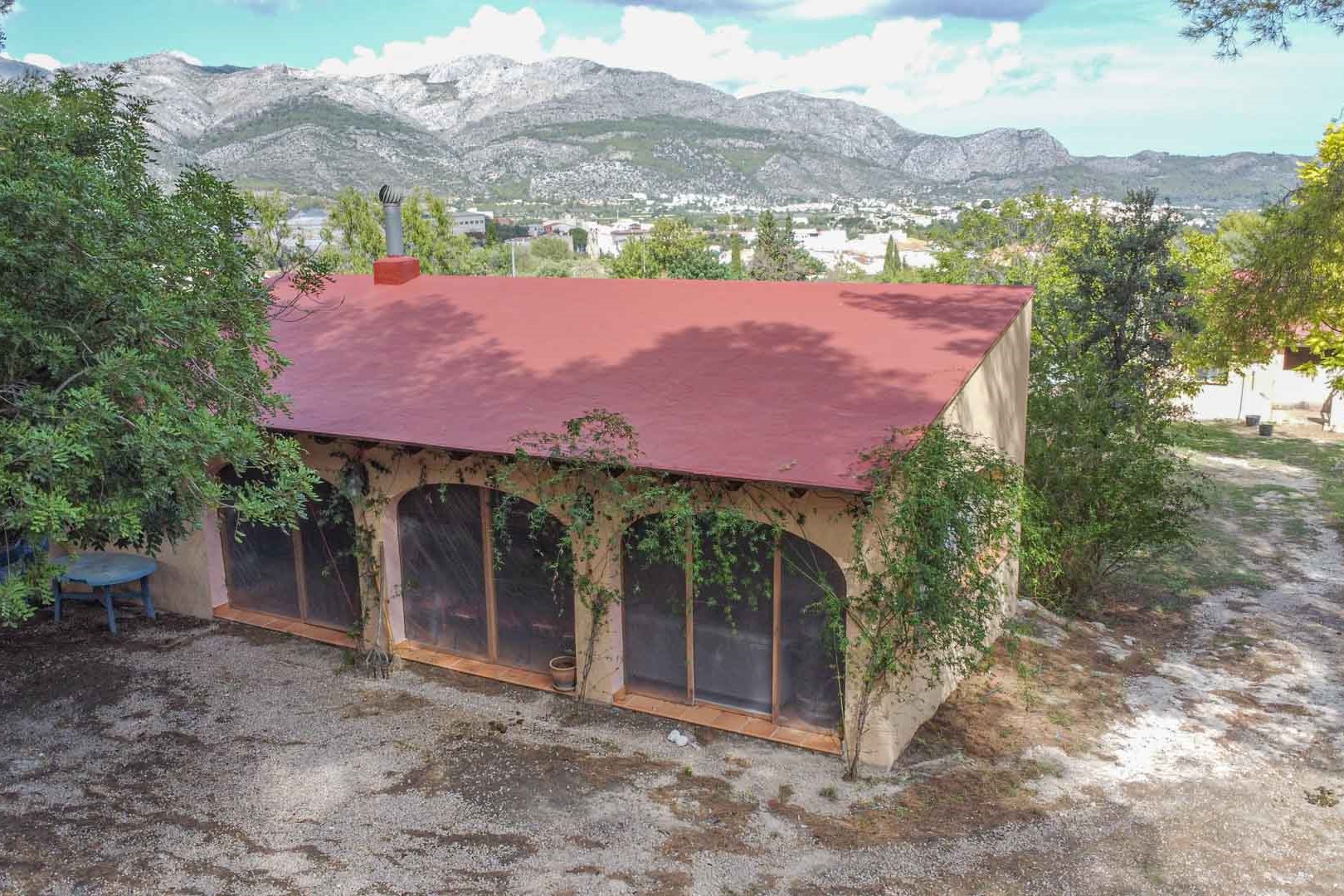 Außenansicht des Nebengebäudes mit bogenförmigen Glasfronten und Schornstein, eingebettet in die Natur mit weitem Blick auf das Tal und die Berge von Orba.