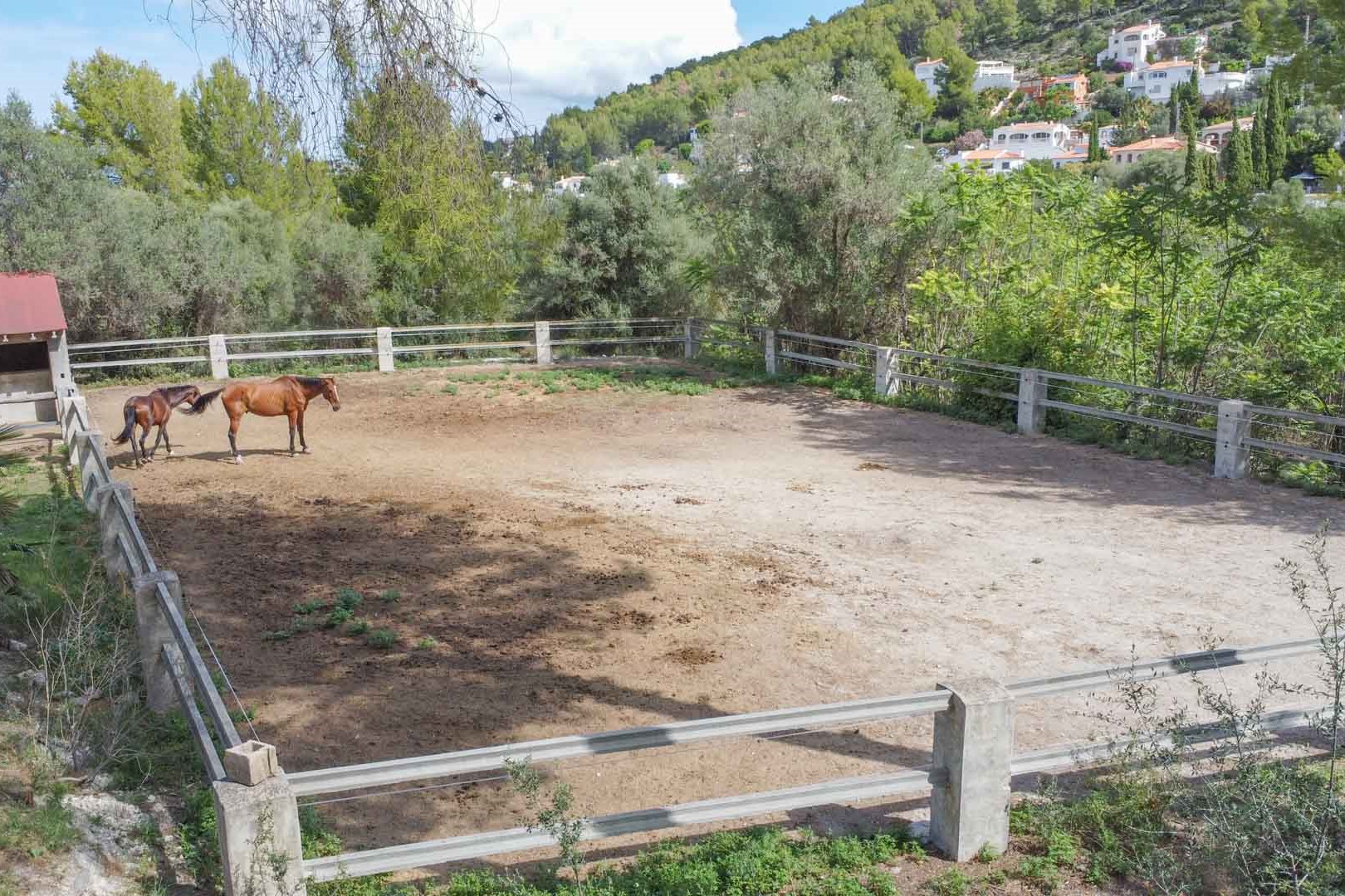 Eingezäunter Reitplatz mit Steinpfosten auf einem weitläufigen Grundstück, umgeben von mediterraner Vegetation und Blick auf die Hügel.