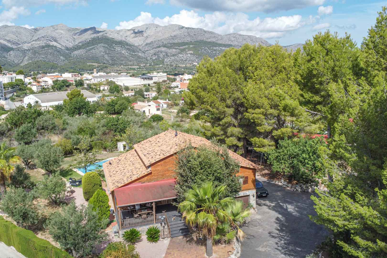 Luftaufnahme der Villa aus finnischem Kiefernholz, eingebettet in mediterrane Gärten mit Blick auf das Tal von Orba und die umliegenden Berge.