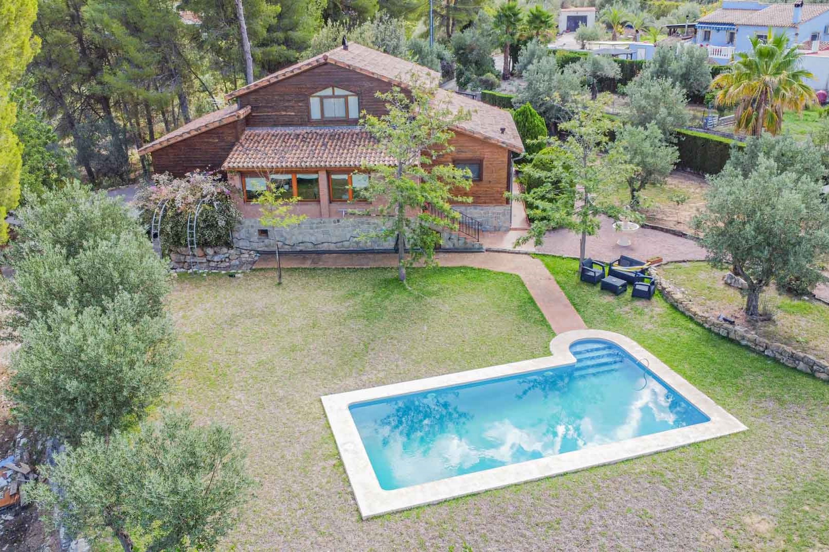 Luftaufnahme der Villa aus Holz und Stein mit privatem Pool, weitläufiger Rasenfläche und mediterranem Garten mit Olivenbäumen.