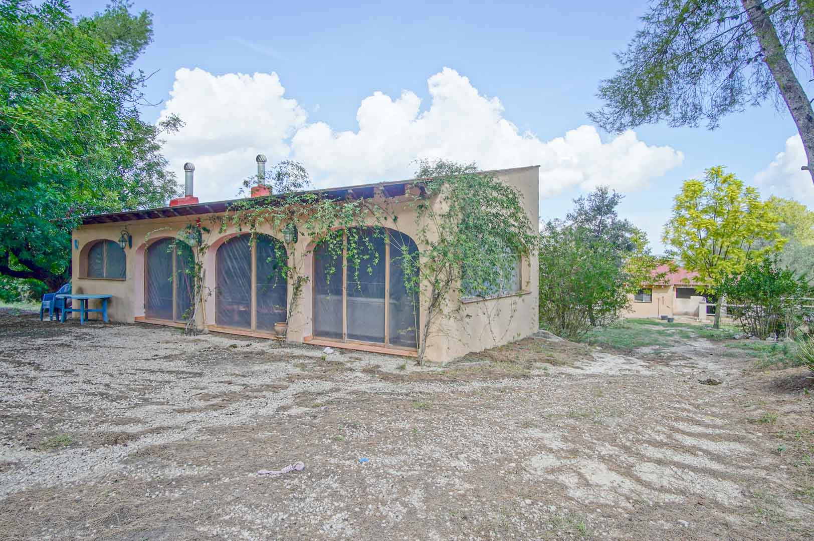 Nebengebäude mit Rundbogenöffnungen und sichtbaren Holzbalken, umgeben von Pinien und mediterraner Vegetation auf dem weitläufigen Naturgrundstück.