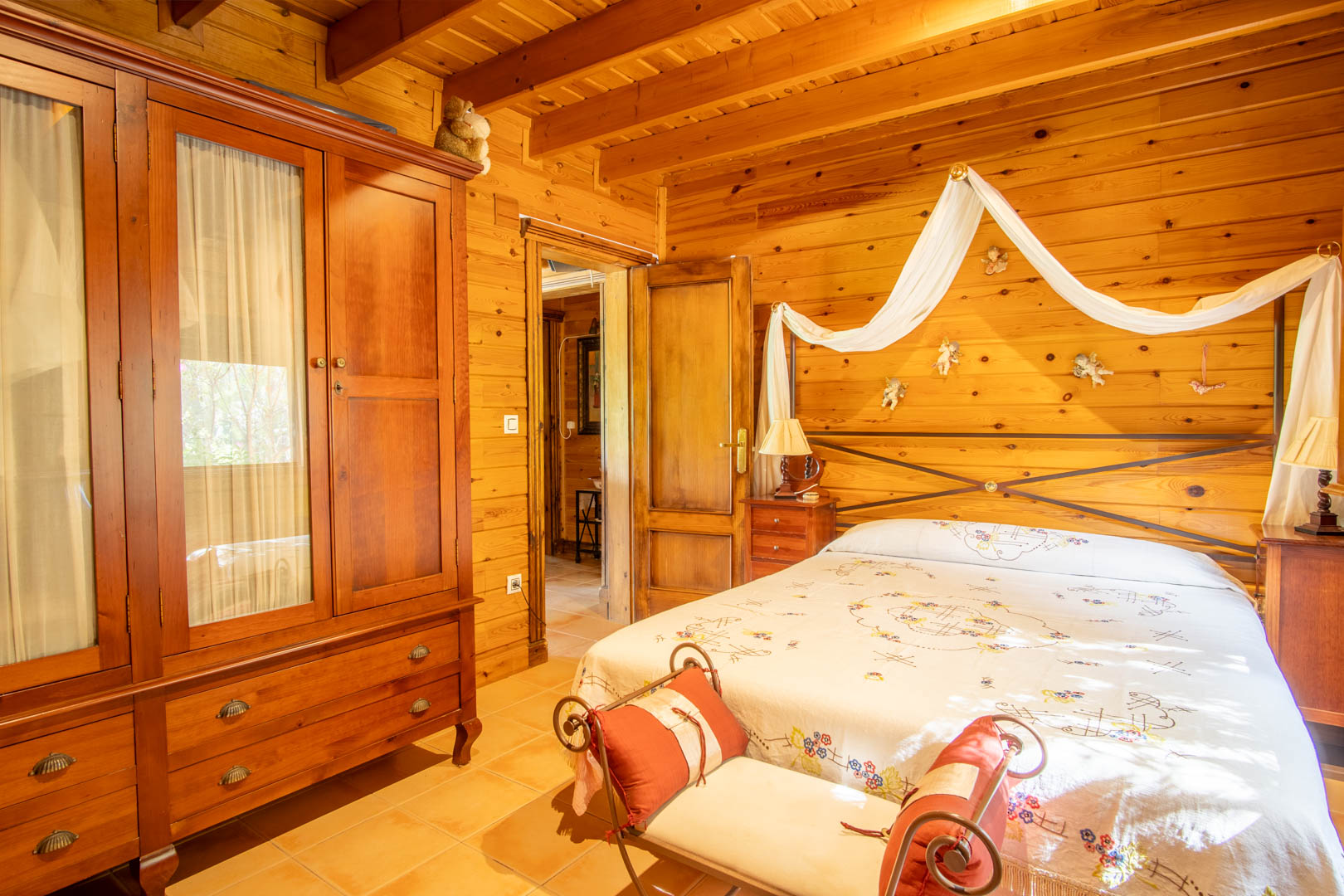 Rustikales Schlafzimmer mit Wänden und Decken aus finnischer Kiefer, einem Massivholzschrank und einem Doppelbett mit dekorativem Baldachin und schmiedeeisernem Kopfteil.