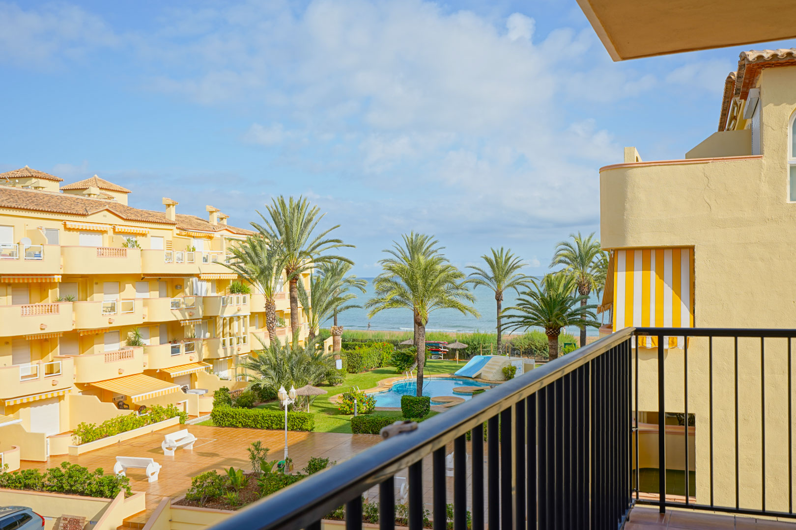 Blick von einem privaten Balkon auf eine gepflegte Wohnanlage mit Pool, Palmen und direktem Ausblick auf das Mittelmeer.