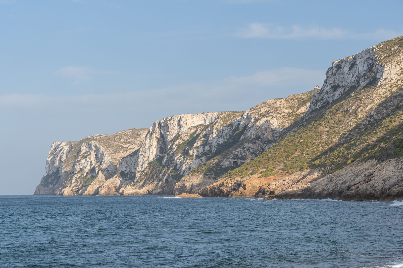 Panoramablick auf schroffe Kalksteinfelsen am Mittelmeer mit natürlichen Felsformationen und spärlicher Küstenvegetation unter klarem Himmel.