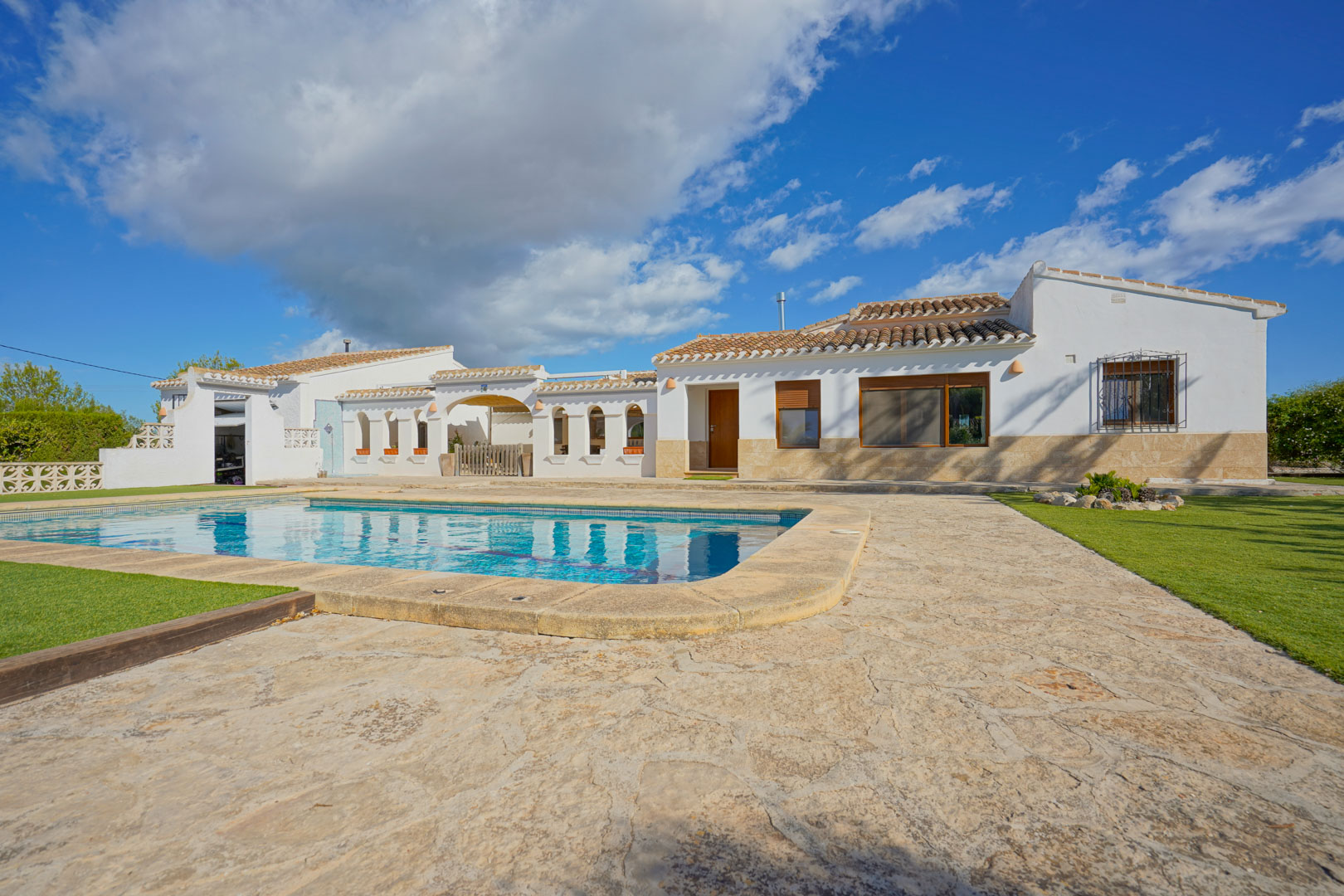 Außenansicht der Villa mit privatem Pool, weitläufiger Natursteinterrasse und gepflegten Rasenflächen im mediterranen Stil.