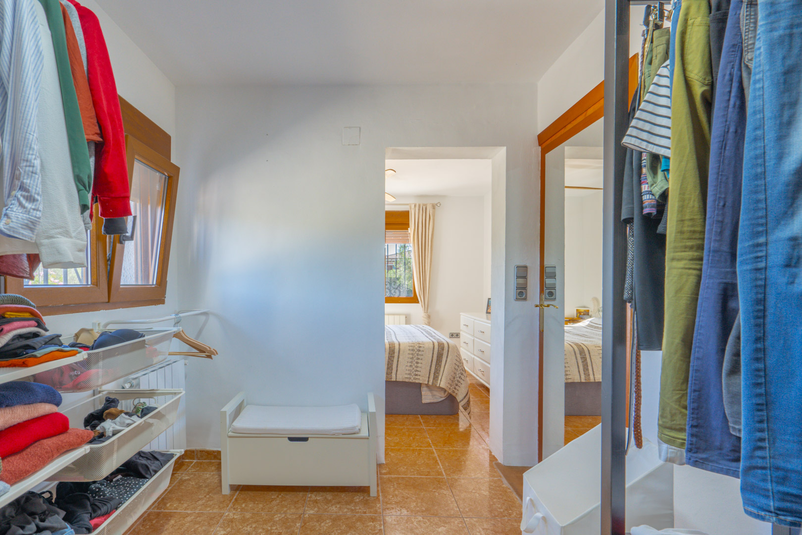 Funktionaler begehbarer Kleiderschrank mit offenen Regalen, Netzschubladen und Kleiderstangen, direkt verbunden mit dem Schlafzimmer mit Fliesenboden.