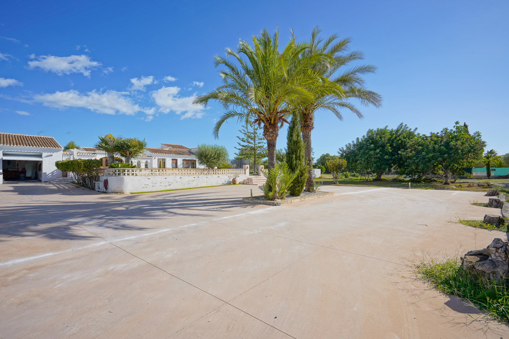 Großzügige gepflasterte Einfahrt mit zentralen Palmen, die direkten Zugang zur Garage und zur weißen Villa im mediterranen Stil bietet.