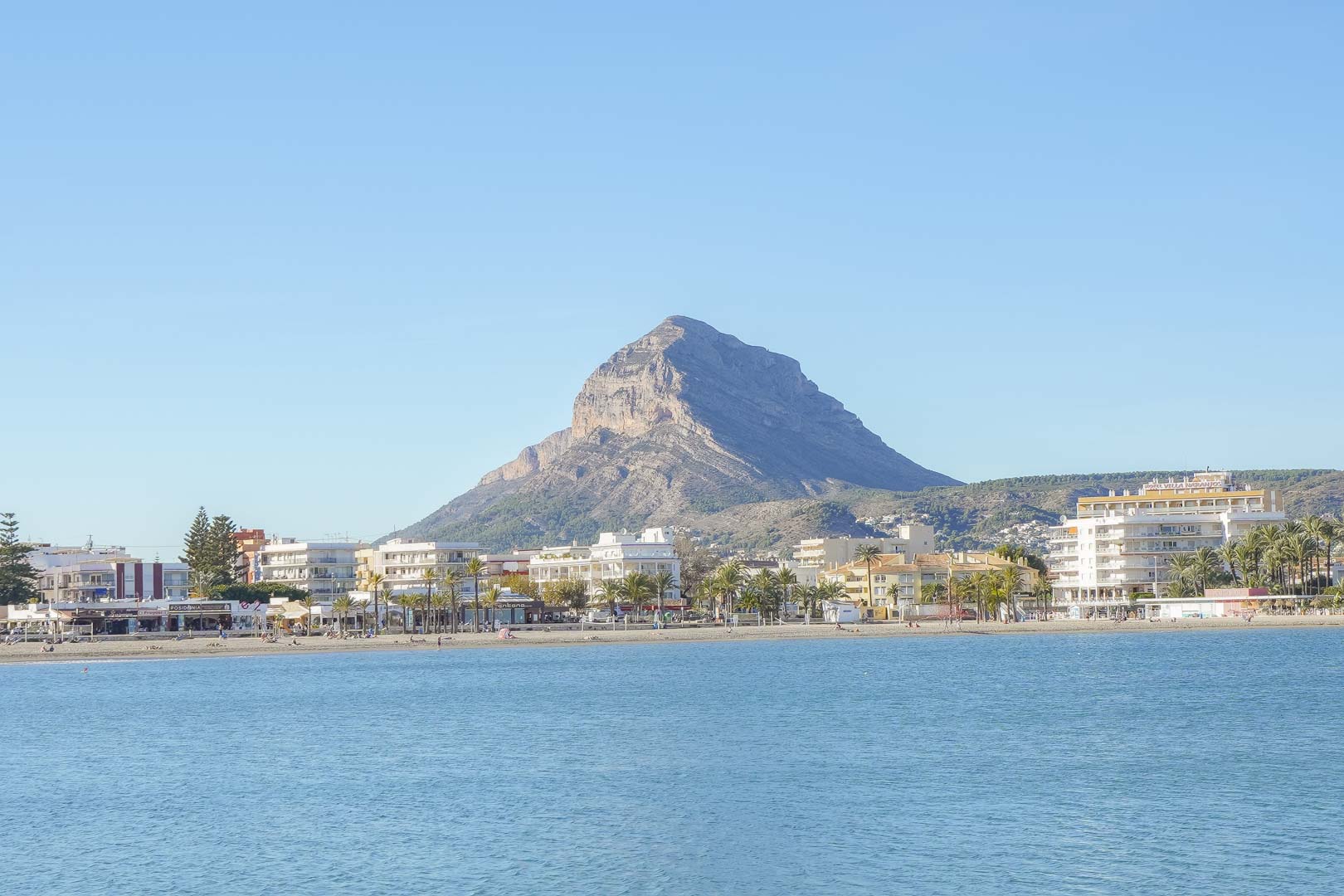 Panoramablick auf den Strand von Arenal in Jávea mit dem markanten Berg Montgó im Hintergrund und der Küstenbebauung am Mittelmeer.