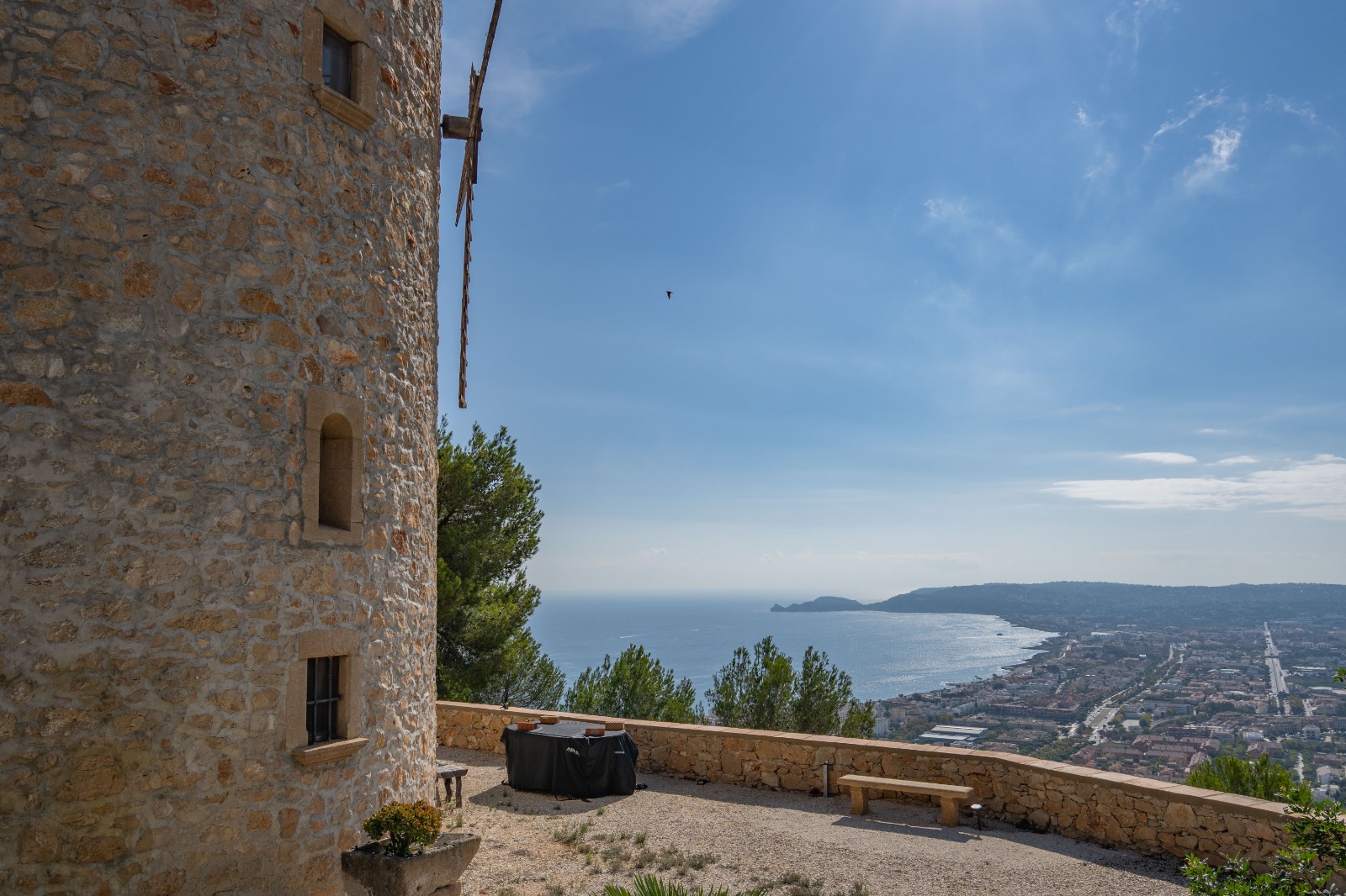 Panoramablick vom Steinturm auf die Bucht von Jávea und das Mittelmeer, mit einer Kiesterrasse und einer Begrenzungsmauer aus Naturstein.