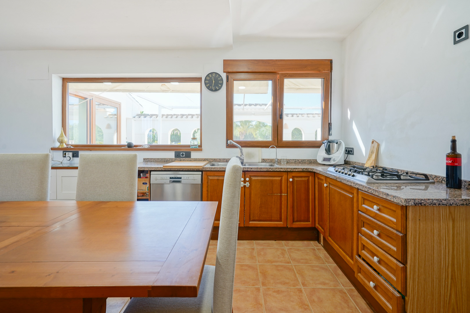 Rustikale Küche mit Granitarbeitsplatten, Holzschränken und Essbereich. Große Fenster bieten Blick auf die Terrasse und sorgen für viel natürliches Licht.