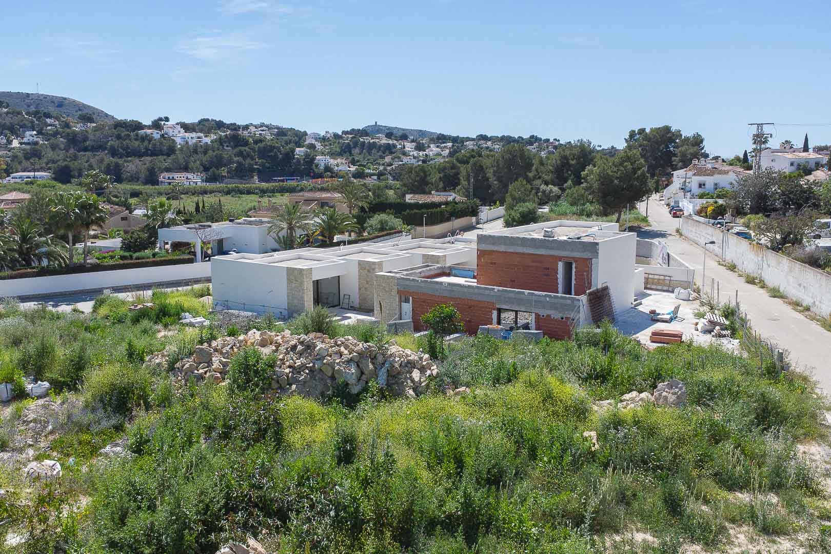 Außenansicht der im Bau befindlichen Villa mit moderner Architektur, Natursteinfassaden und Ziegelwänden in einer mediterranen Hügellandschaft.
