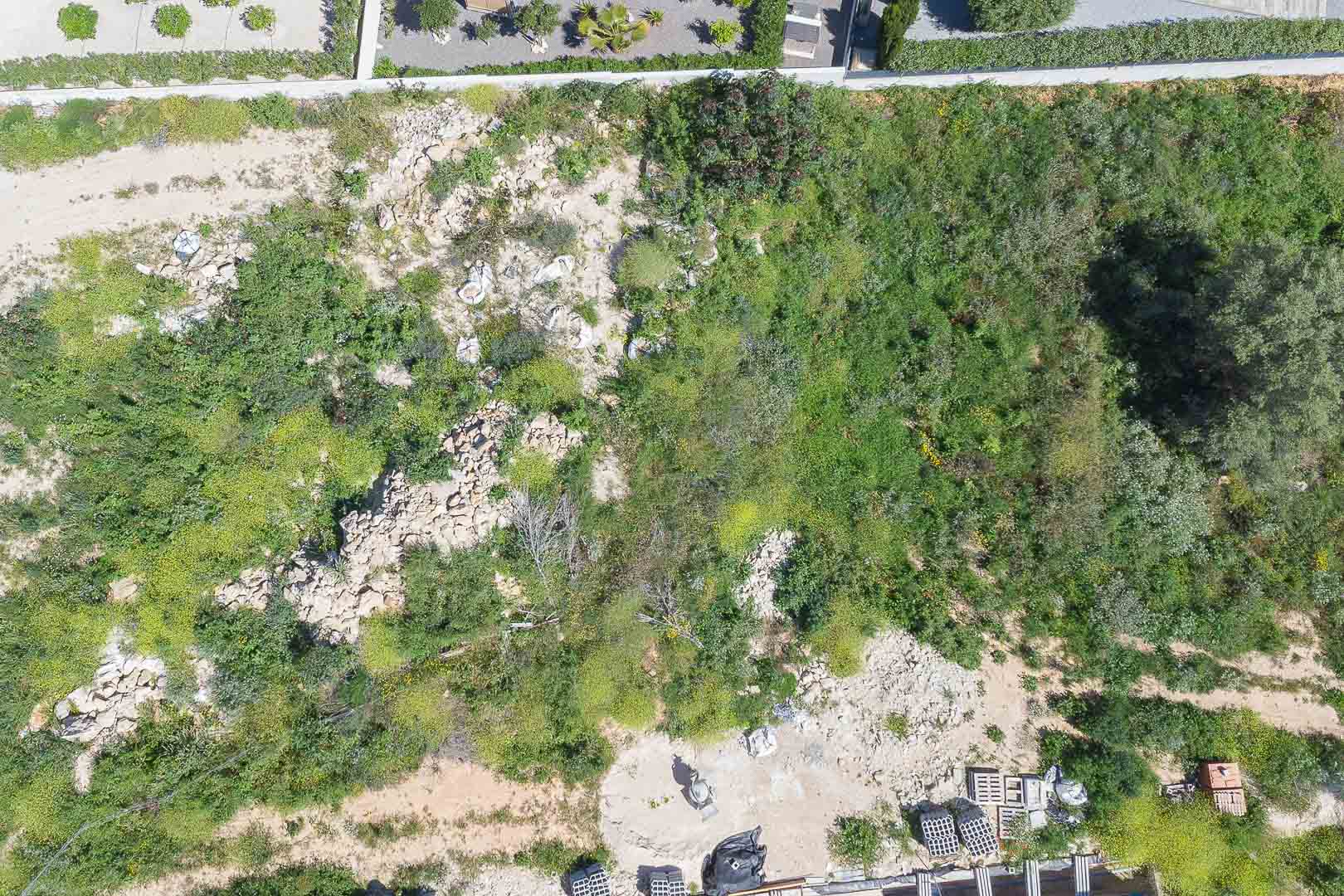 Draufsicht auf das über 1.000 m² große Grundstück mit natürlicher mediterraner Vegetation und ersten Baumaterialien vor Ort.