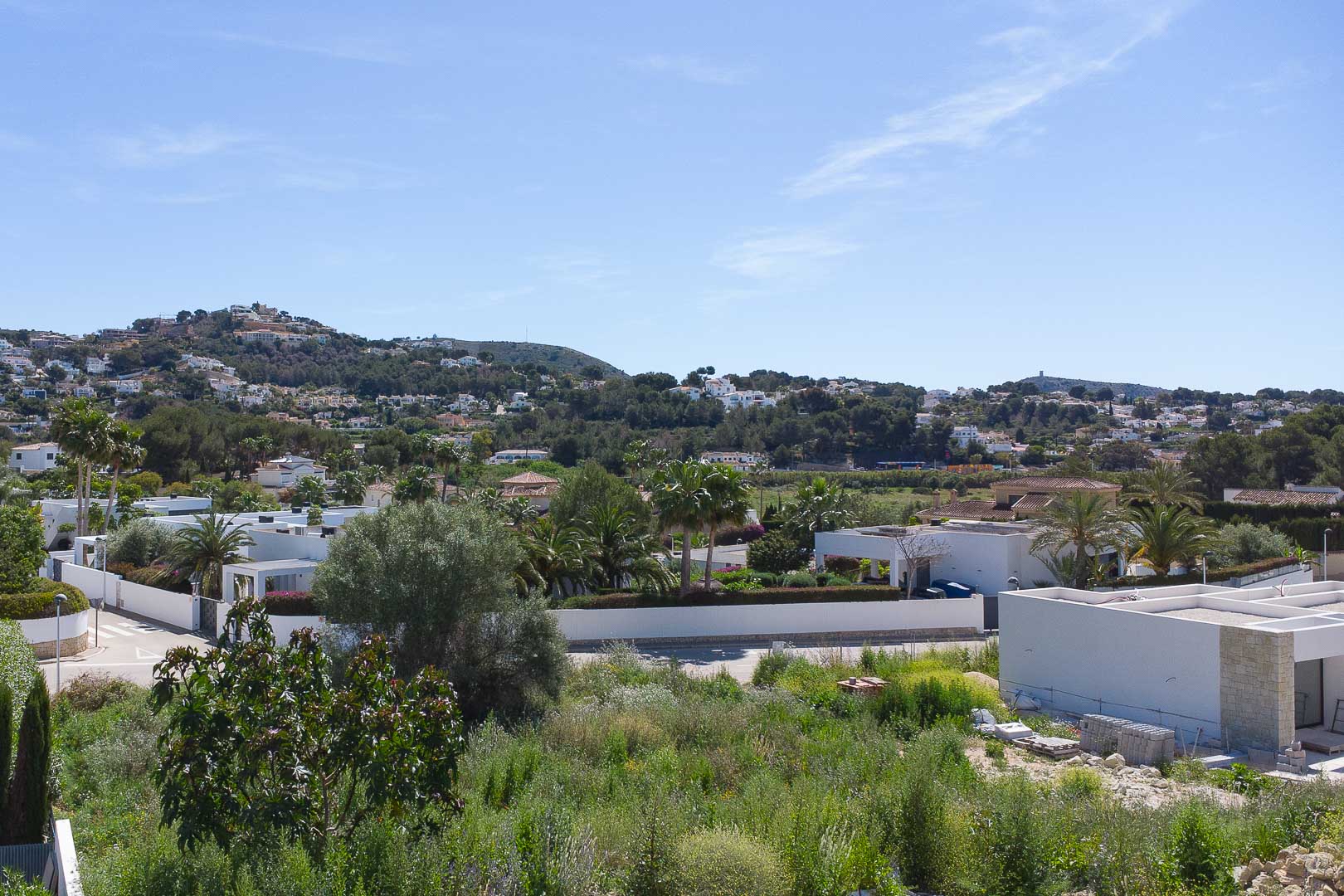 Erhöhter Panoramablick auf das Wohngebiet von Moraira mit modernen weißen Villen, eingebettet in die mediterrane Landschaft und üppige Vegetation.