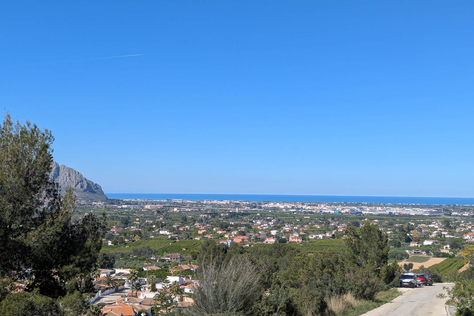 Panoramablick auf Pedreguer mit dem Mittelmeer im Hintergrund und üppigem Grün im Vordergrund.