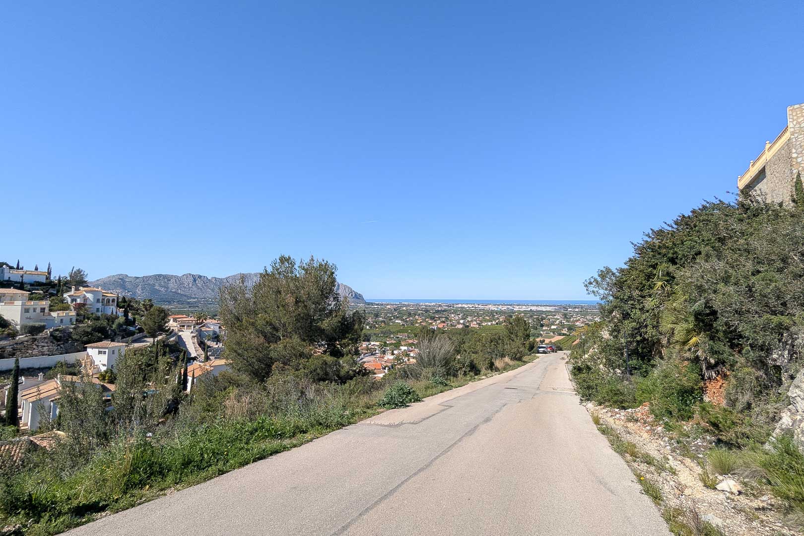 Zufahrtsstraße zur Villa mit Panoramablick auf Pedreguer und das Mittelmeer am Horizont unter klarem Himmel.