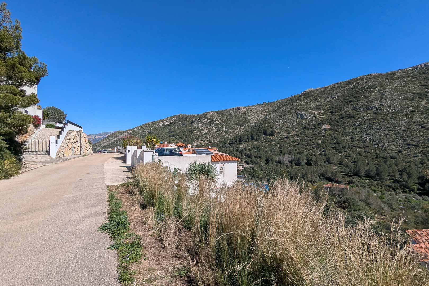 Außenansicht der Villa vom Zufahrtsweg aus, mit Sonnenkollektoren auf dem Dach und der natürlichen Berglandschaft von Pedreguer im Hintergrund.