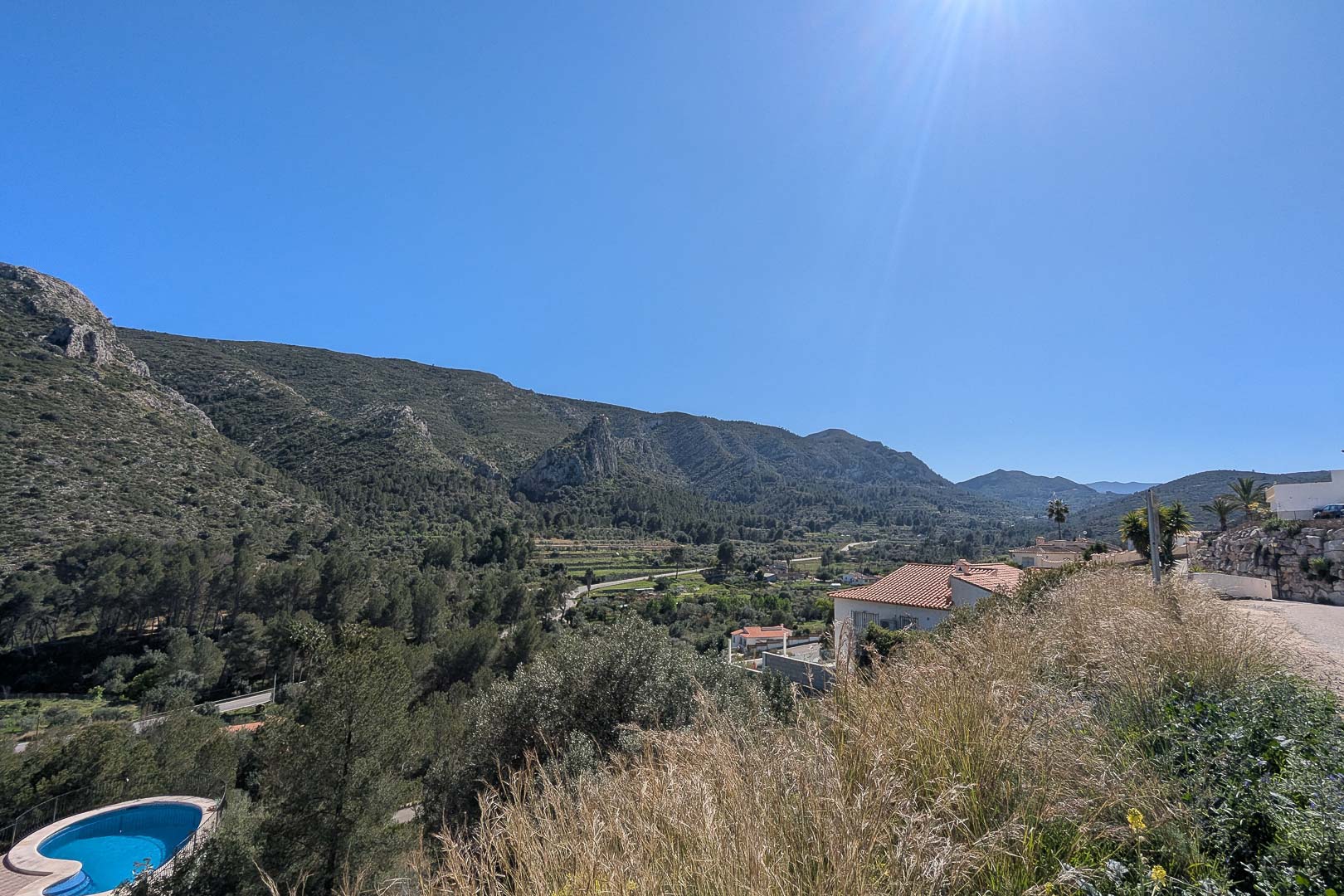 Erhöhter Panoramablick auf das Tal von Pedreguer und die umliegenden Berge, der die natürliche mediterrane Landschaft unter strahlend blauem Himmel zeigt.