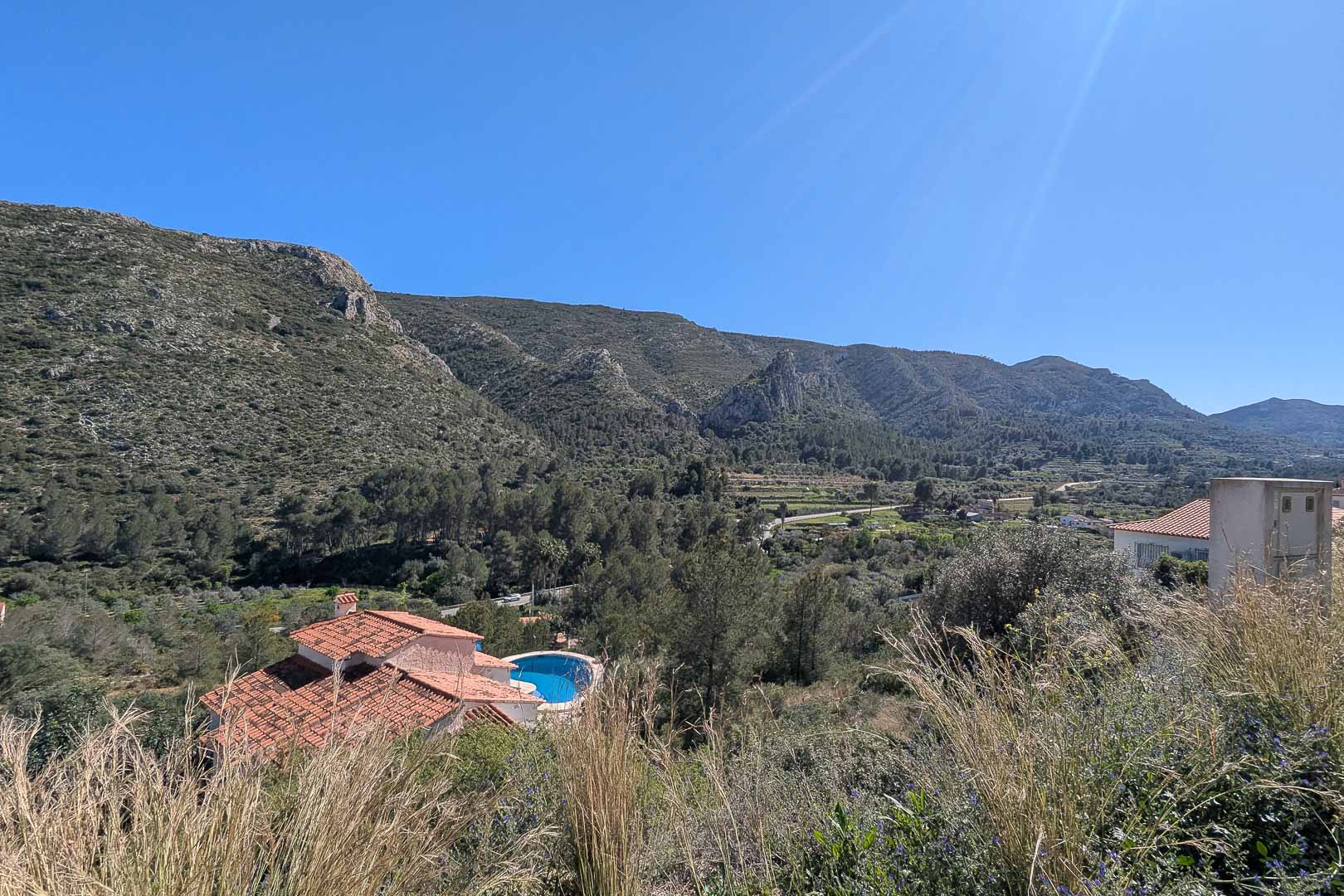 Erhöhter Panoramablick über das Tal und die Berge von Pedreguer, umgeben von mediterraner Vegetation und Blick auf einen Pool in der Nachbarschaft.