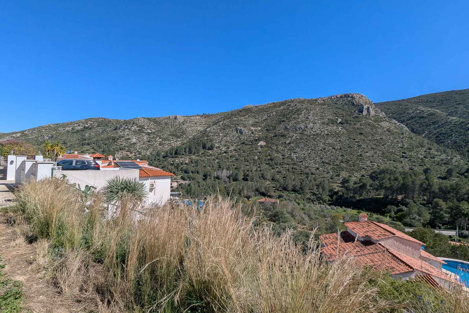 Panoramablick auf die Berge und das Tal vom Grundstück aus, der die natürliche mediterrane Landschaft und die benachbarten Villen zeigt.