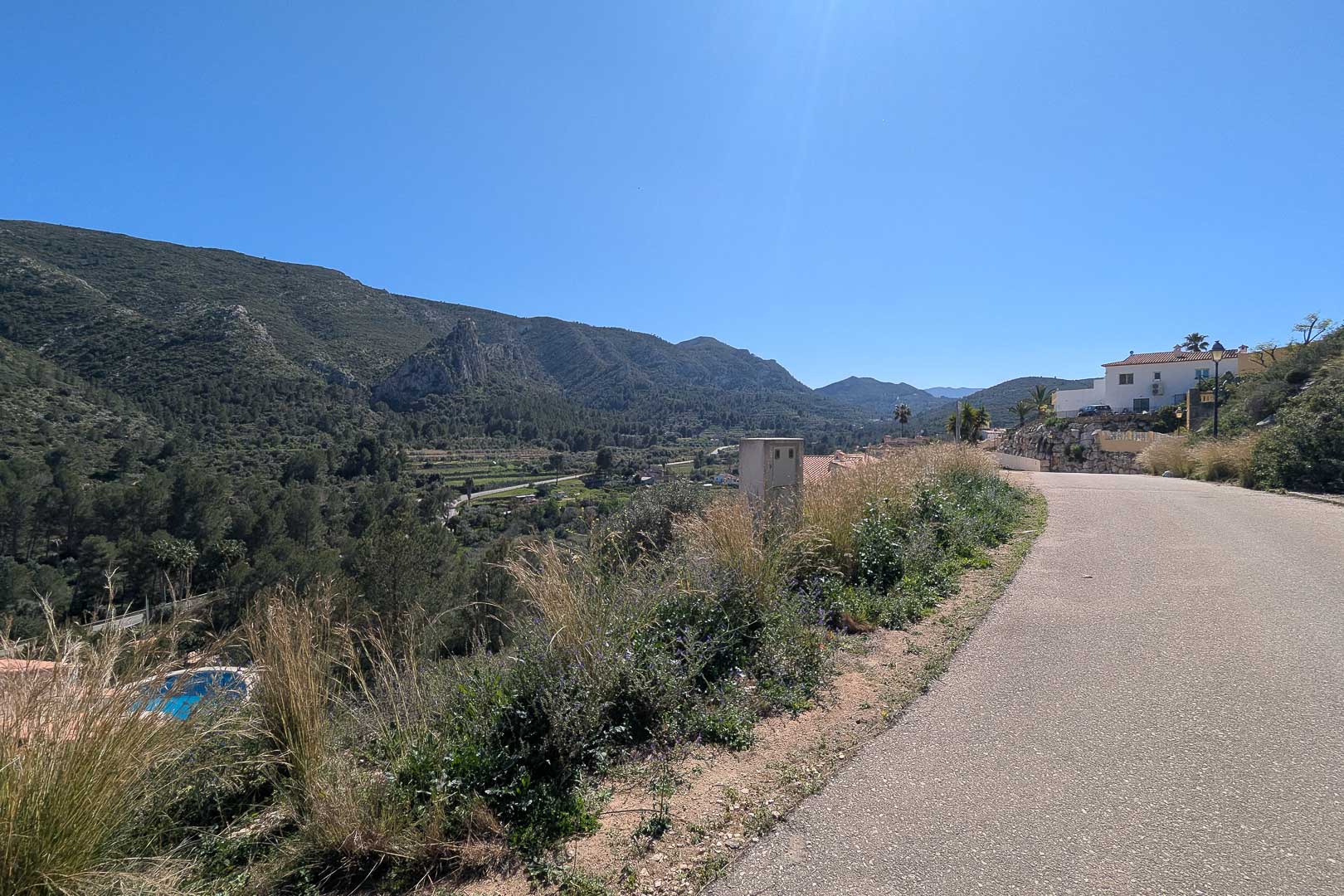 Panoramablick von der Zufahrtsstraße auf das Tal und die umliegenden Berge von Pedreguer unter strahlend blauem Himmel.
