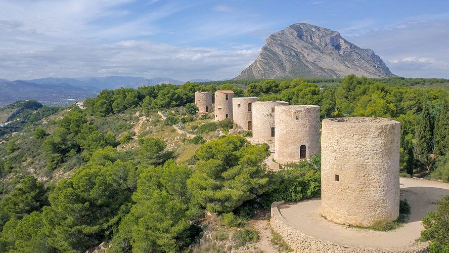 Luftaufnahme der ikonischen Steinwindmühlen in Jávea mit dem imposanten Montgó-Massiv, das die umgebende Naturlandschaft überragt.