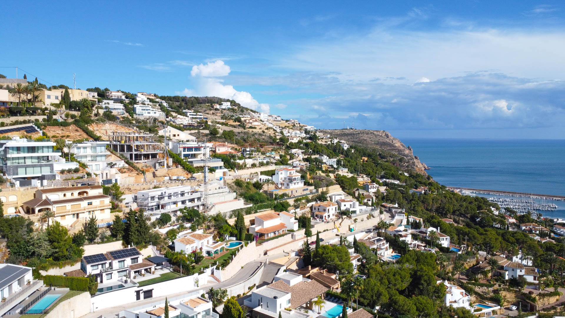 Luftaufnahme des Wohngebiets La Corona in Jávea, die die Hanglage der Villen und die Nähe zum Mittelmeer und dem Hafen zeigt.