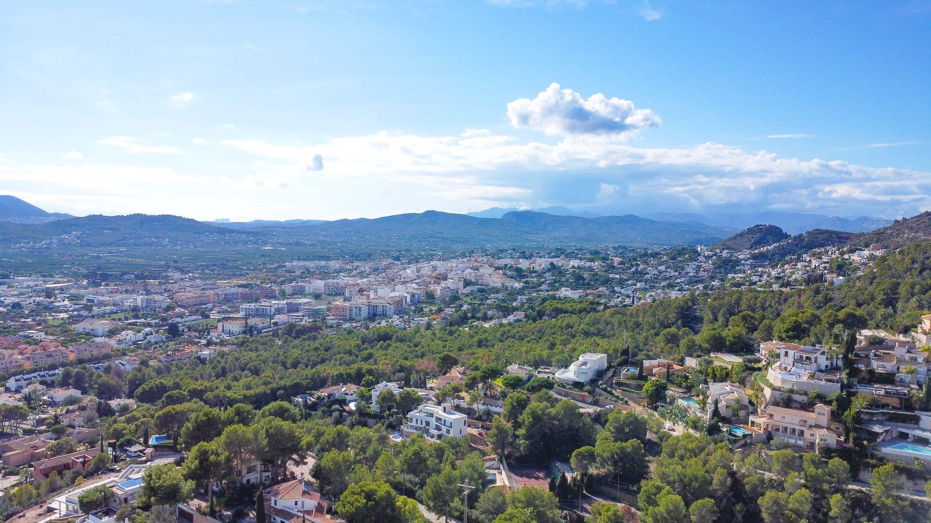 Panorama-Luftaufnahme von La Corona aus, die die umliegenden Pinienwälder und das Stadtgebiet von Jávea vor der markanten Bergkulisse am Horizont zeigt.