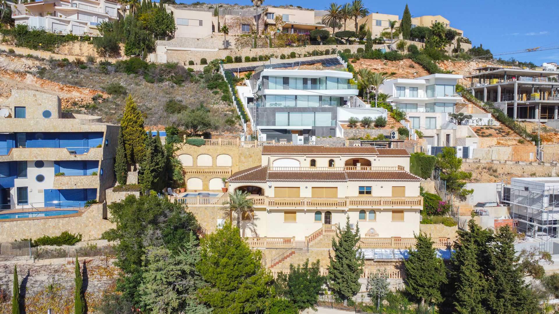 Außenansicht der traditionellen Villa in La Corona mit cremefarbener Fassade, Terrakotta-Ziegeldächern und in den Steilhang integrierten Terrassenebenen mit Balustraden.