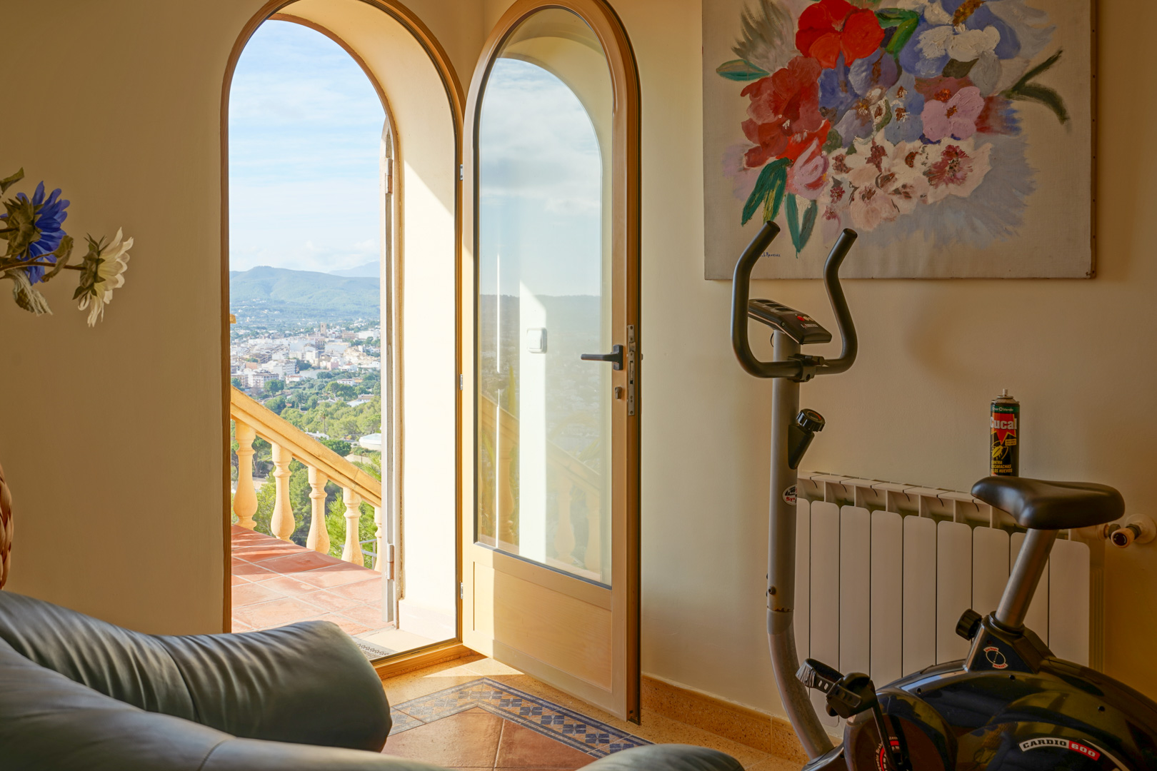 Innenraum mit Heimtrainer und Rundbogentüren, die auf eine Terrasse mit Panoramablick über die Stadt und die umliegende Berglandschaft führen.