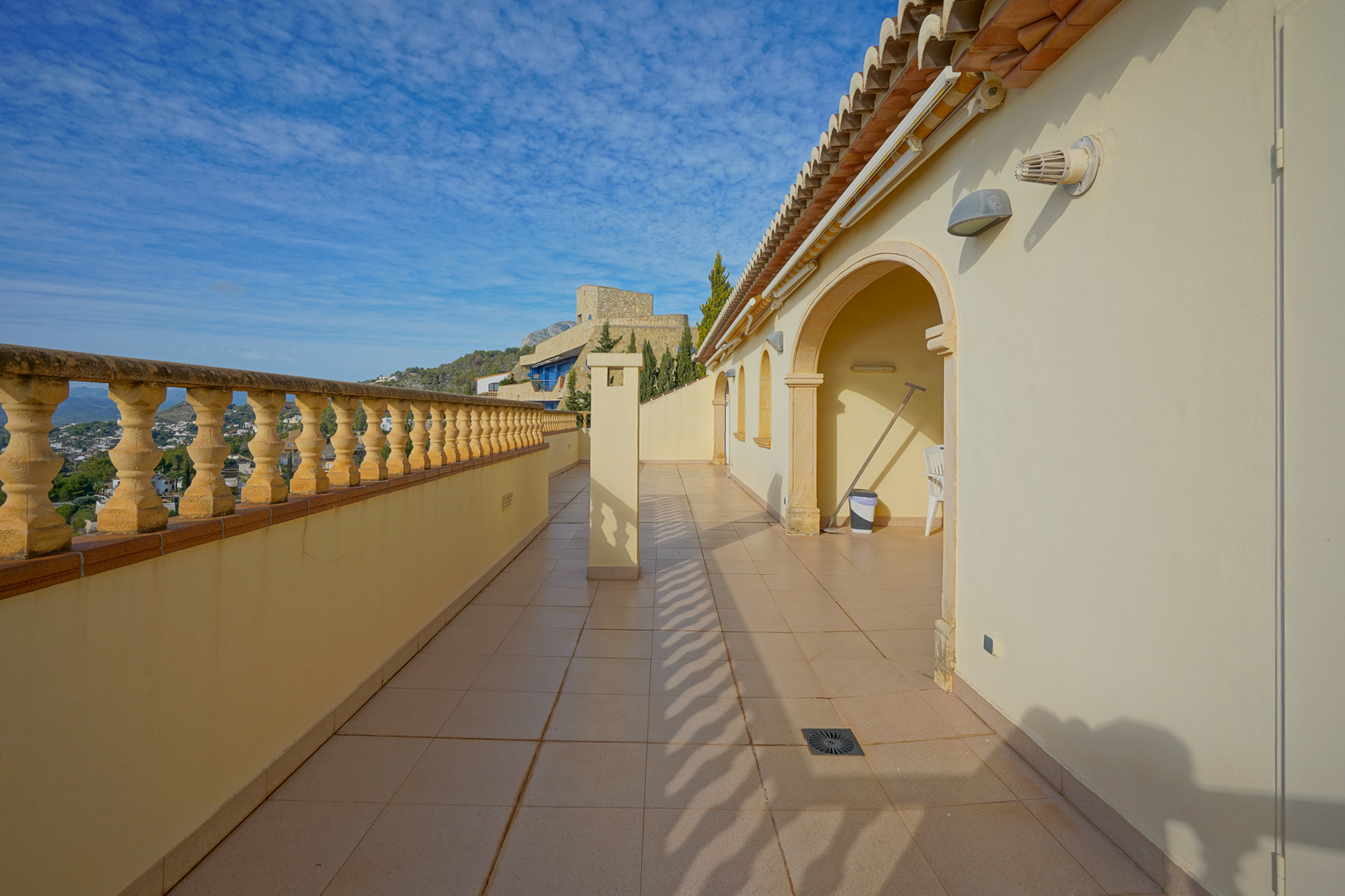 Lange Terrasse mit traditioneller Balustrade, Fliesenboden und Rundbogen-Elementen, die einen weiten Blick über das Tal und die umliegende Landschaft bietet.