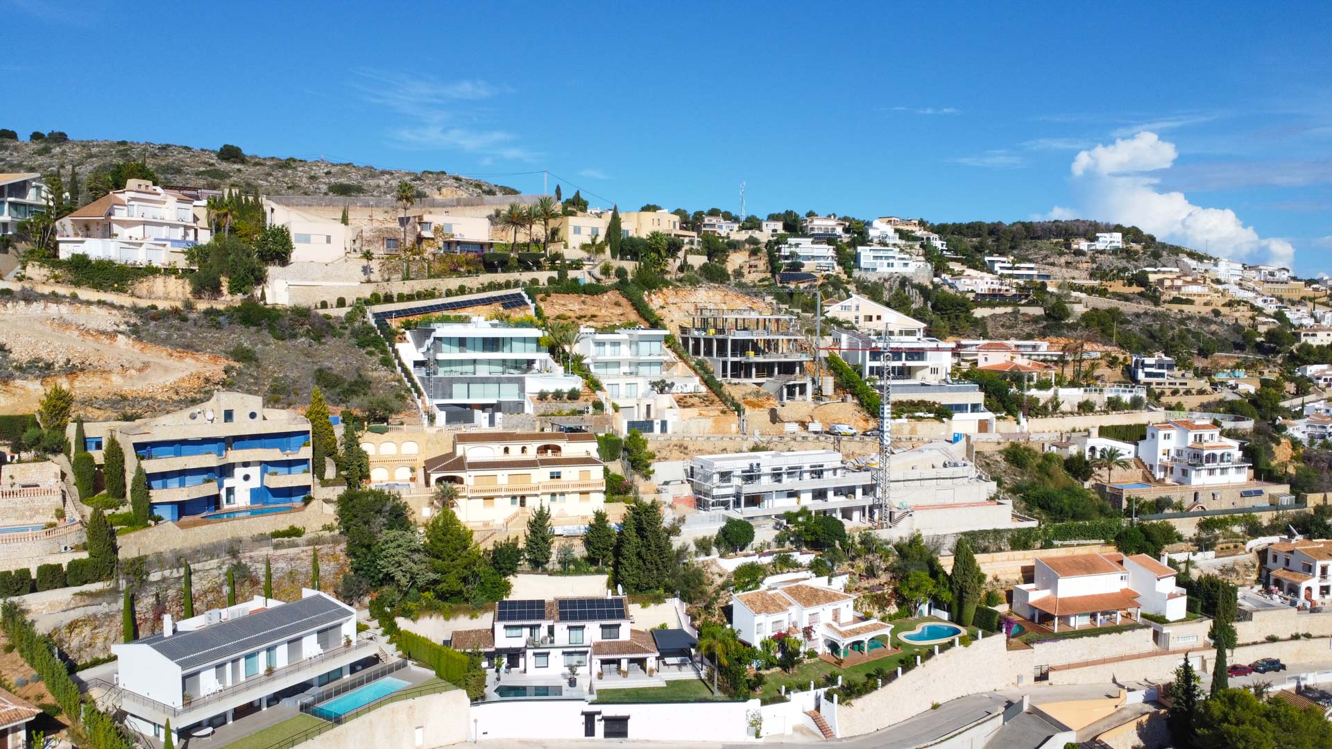 Luftaufnahme der Wohnanlage La Corona in Jávea, die die terrassenförmige Anordnung der Villen am Hang und die vielfältige Architektur der Region zeigt.