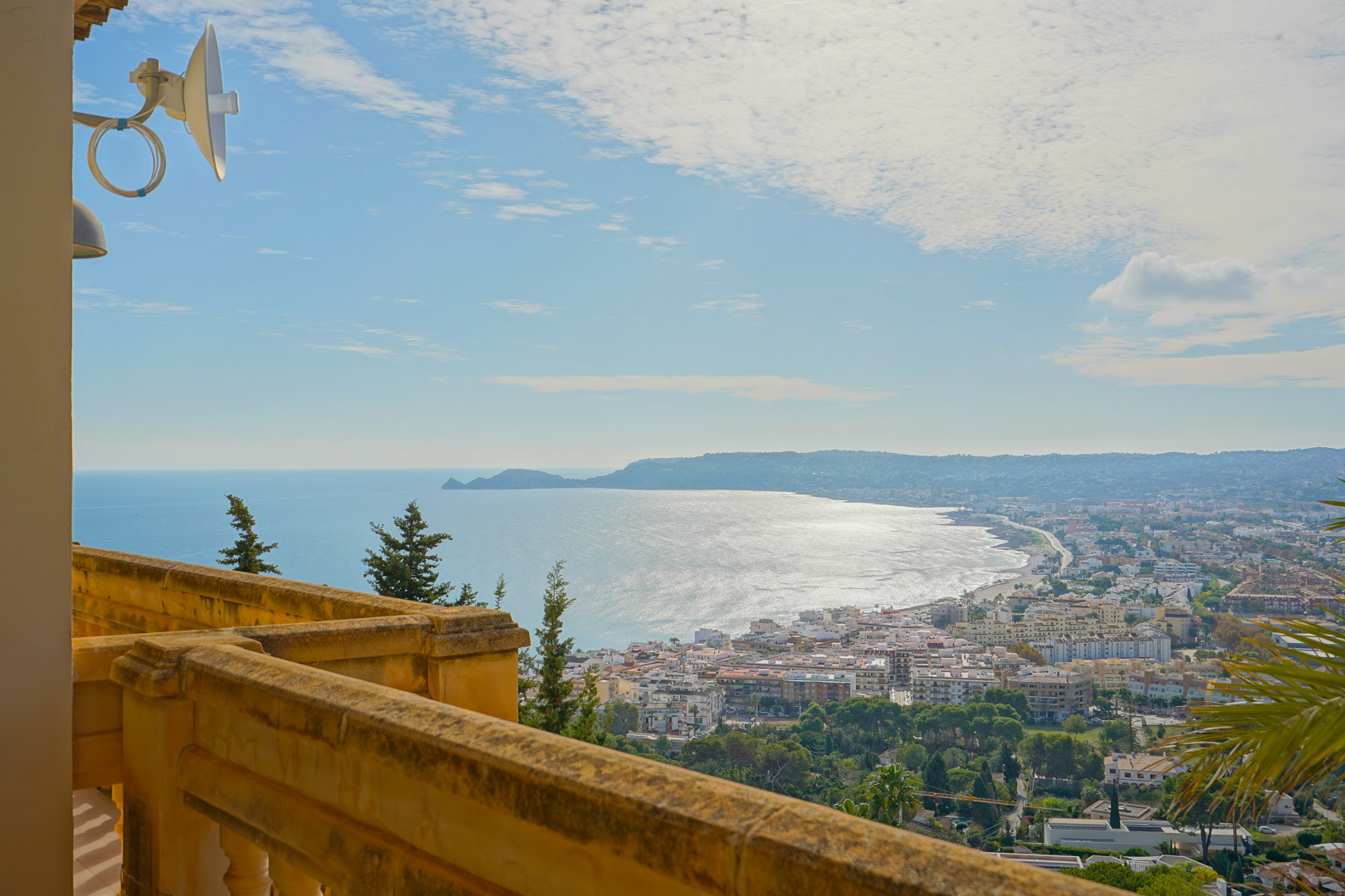 Panoramablick von der Terrasse mit Steinbalustrade über die Bucht von Jávea, den Hafen und die Silhouette des Cap Negre am Horizont.