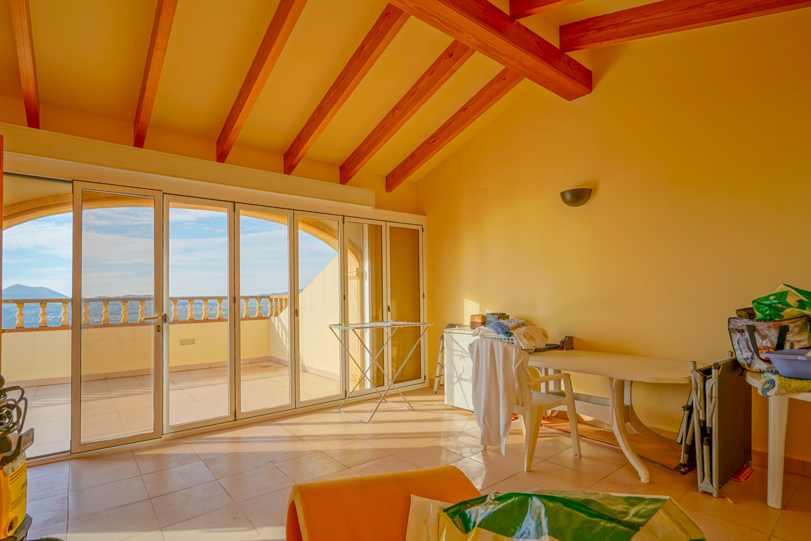 Raum im Obergeschoss mit hohen Decken, sichtbaren Holzbalken und großen Glastüren, die auf eine Terrasse mit weitem Blick auf die Berglandschaft führen.
