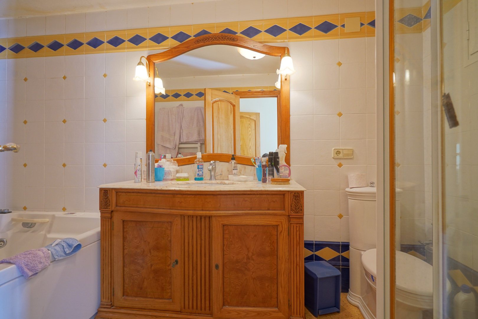 Traditionelles Badezimmer mit einem Waschtisch aus geschnitztem Holz, Marmorplatte und dekorativen Wandfliesen mit blau-gelben Akzenten.